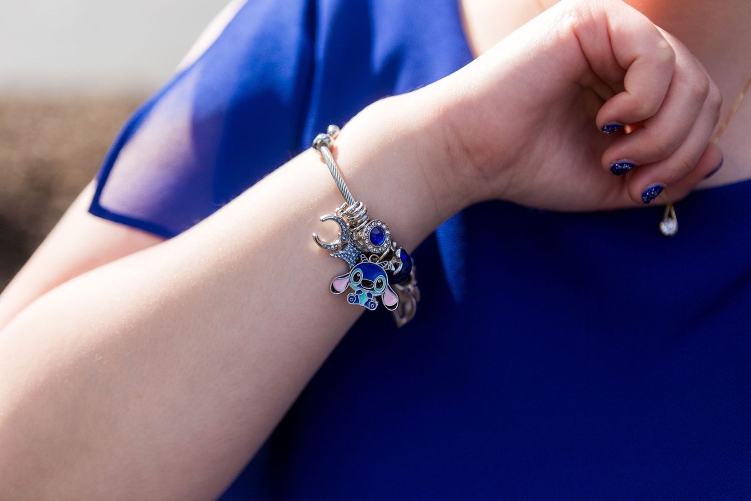 A silver charm bracelet with blue crystal flower dangles against a royal blue background.
