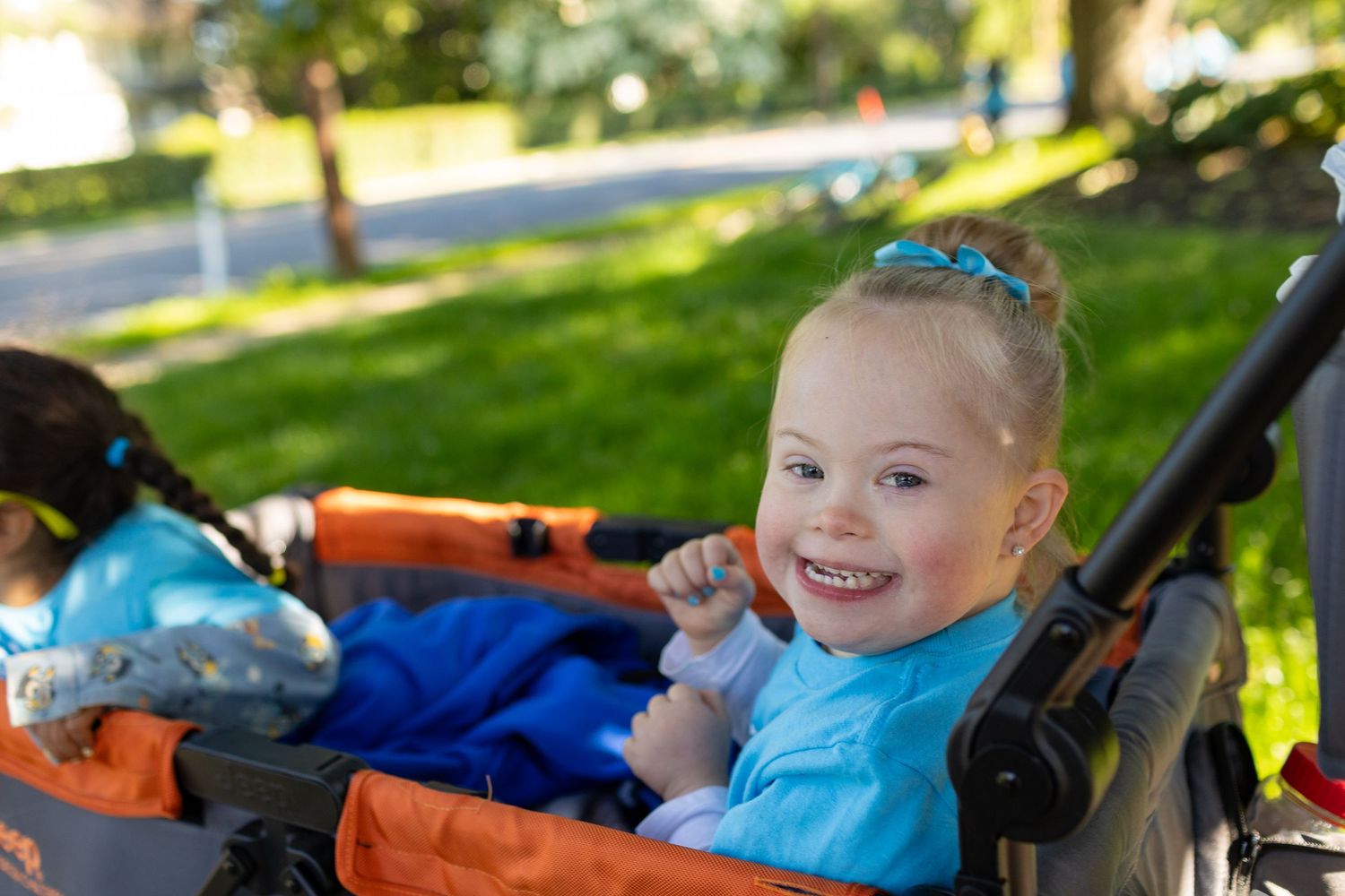 Child in blue shirt smiling while sitting in stroller outdoors.