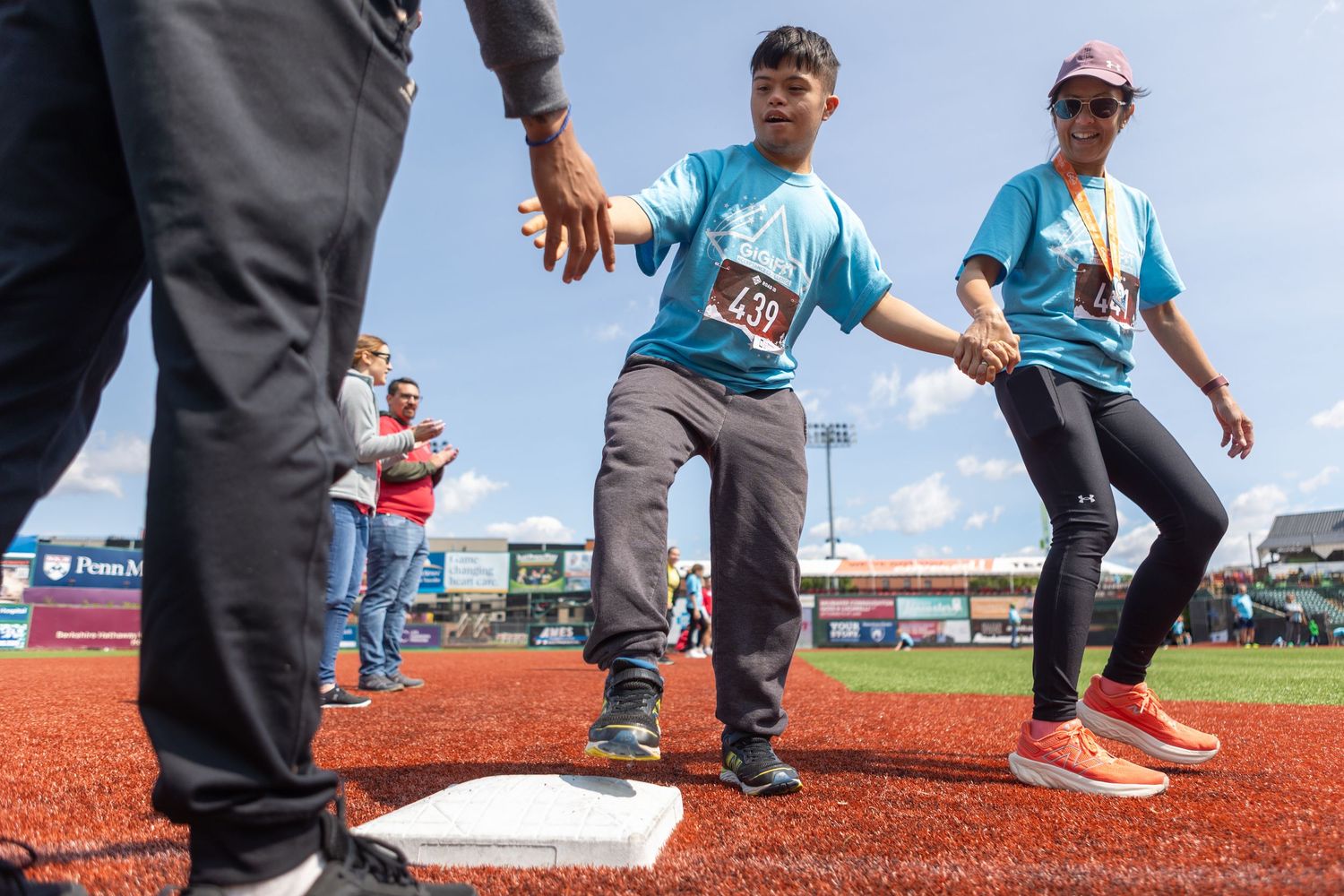 Participants running across bases during charity event at baseball stadium.