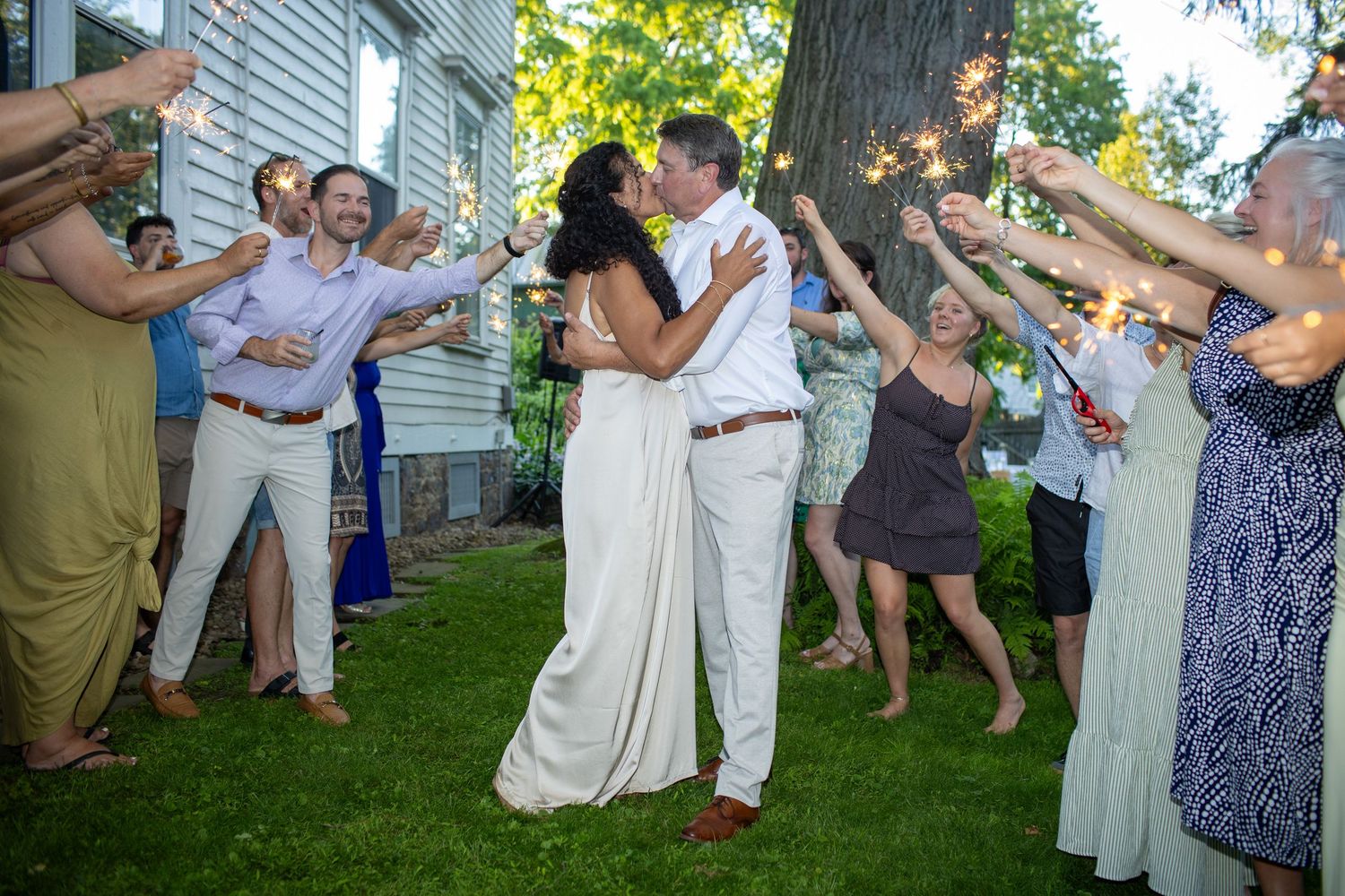 Wedding guests cheer and celebrate as newlyweds share their first kiss in an outdoor garden reception.