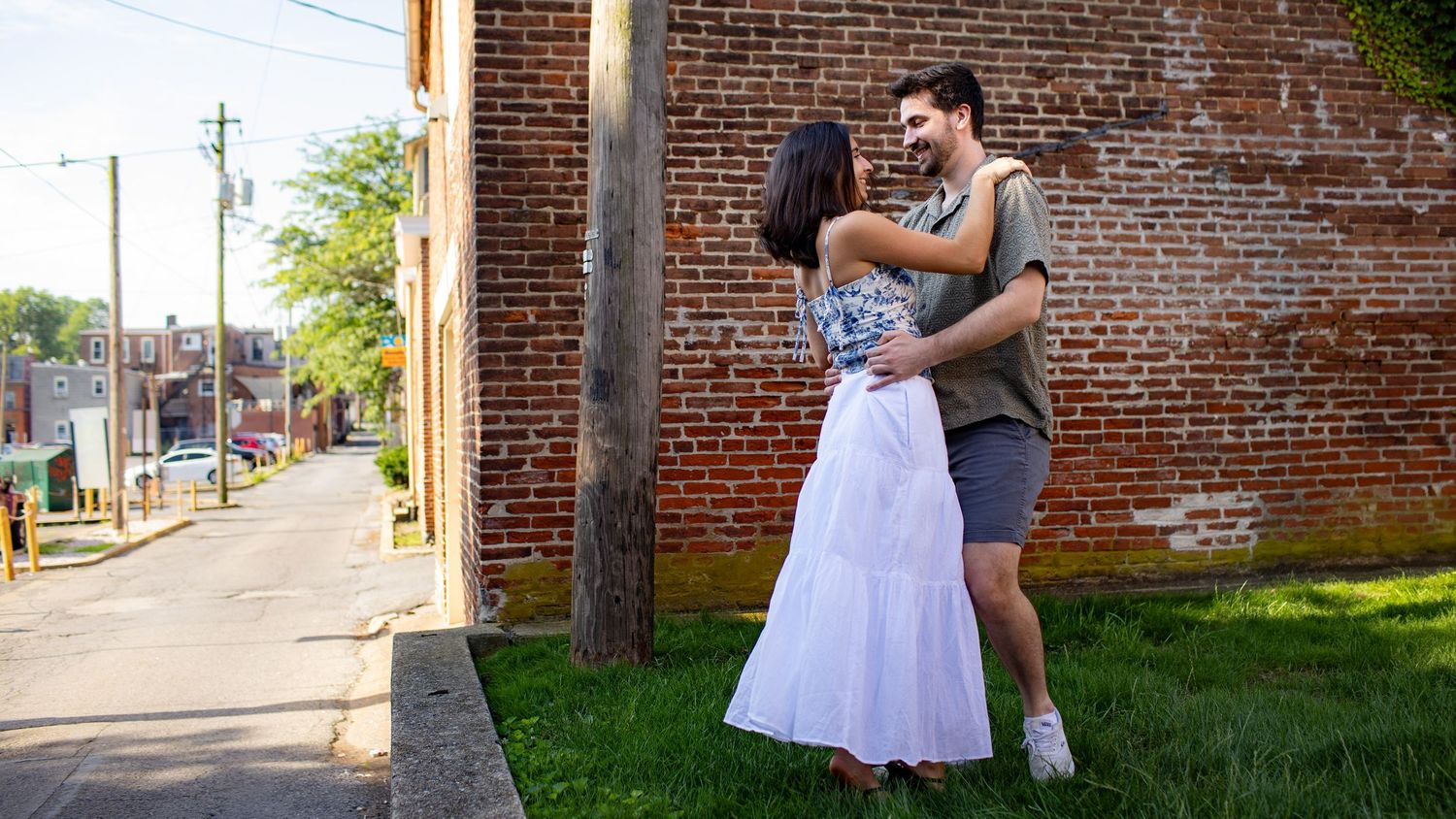 A couple shares an intimate dance against a rustic brick wall backdrop in sunny weather.