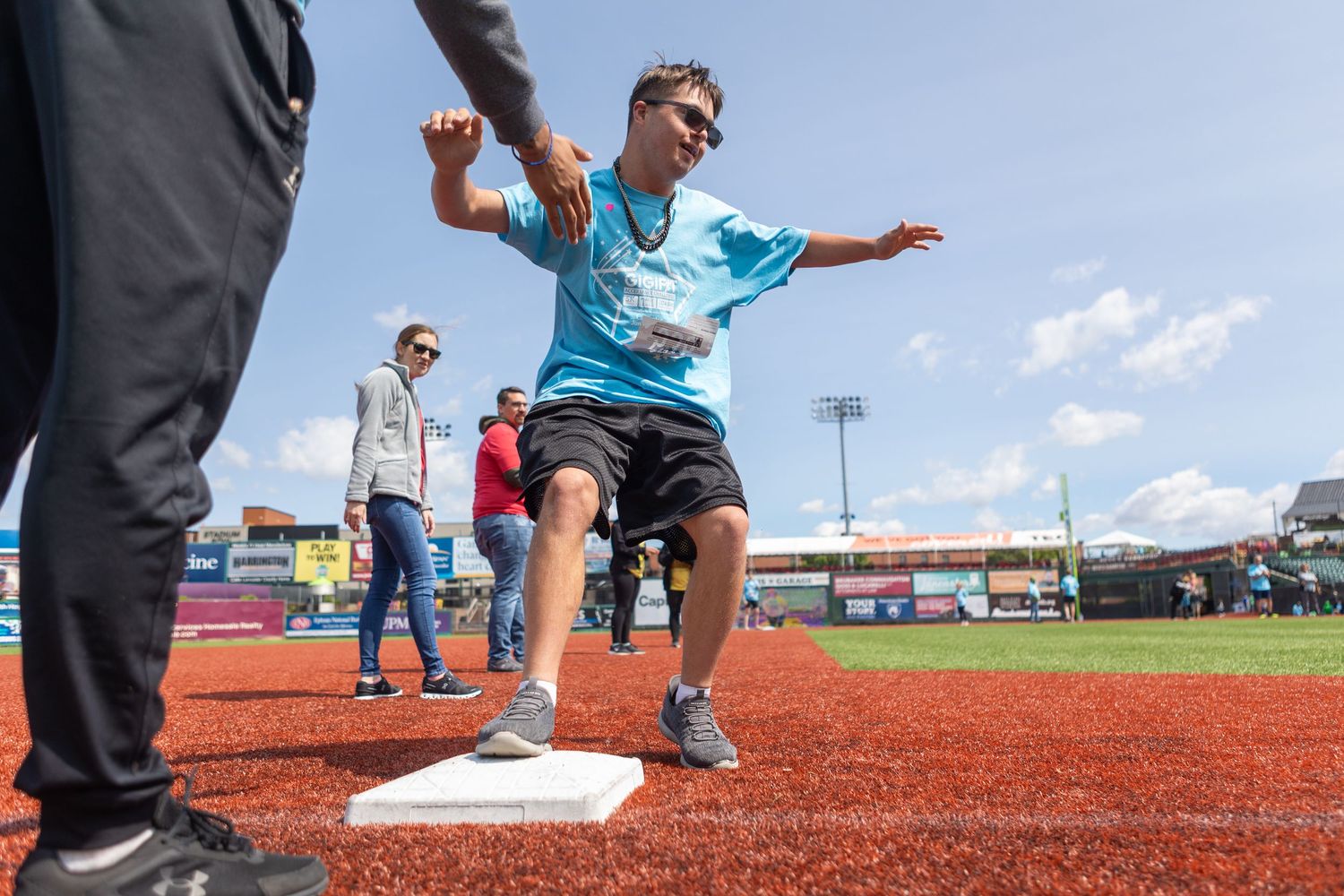 Participants enjoying activities on a red turf baseball field under blue skies.