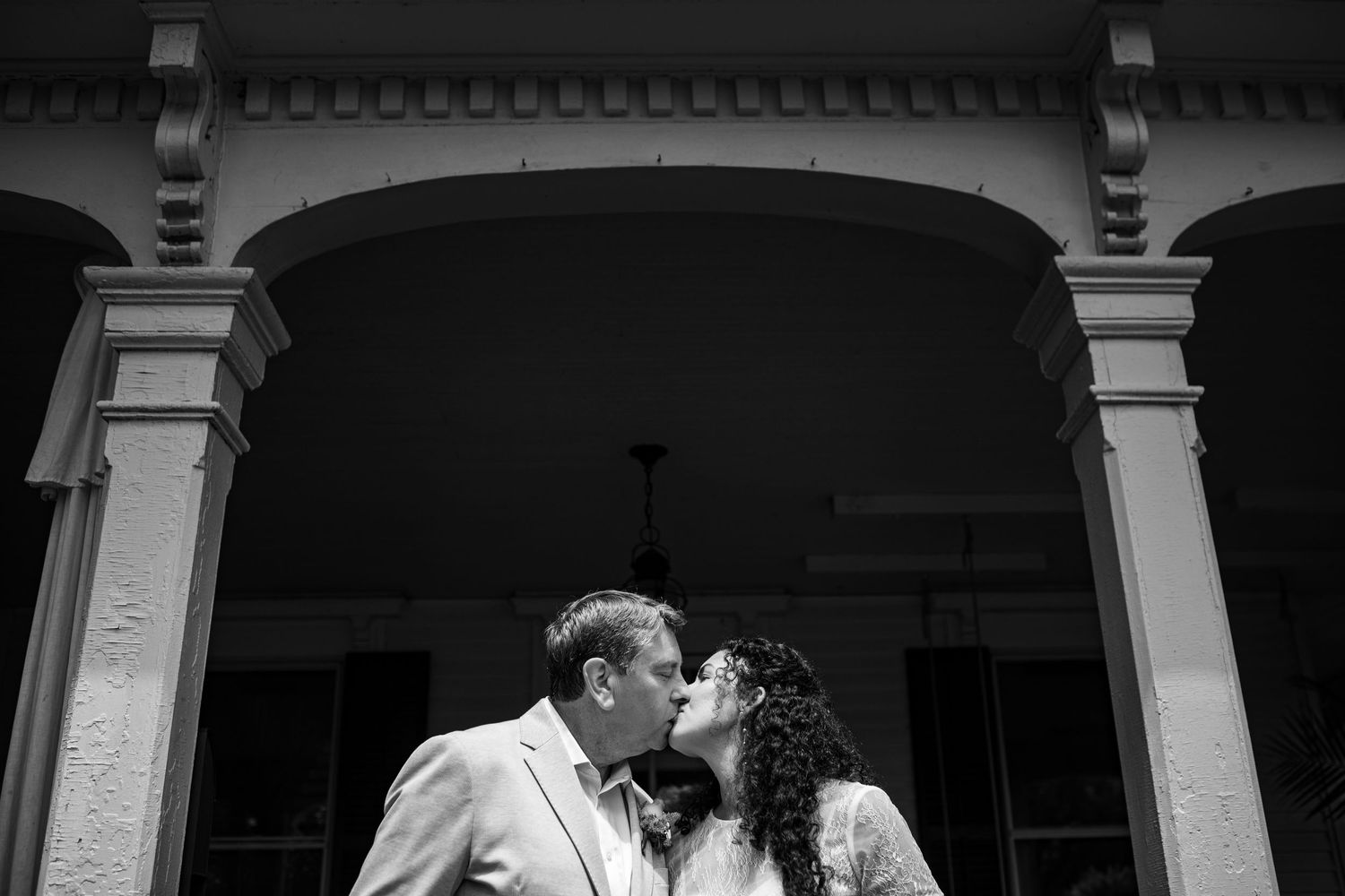A dramatic black and white wedding photo showing a couple kissing under an elegant archway.