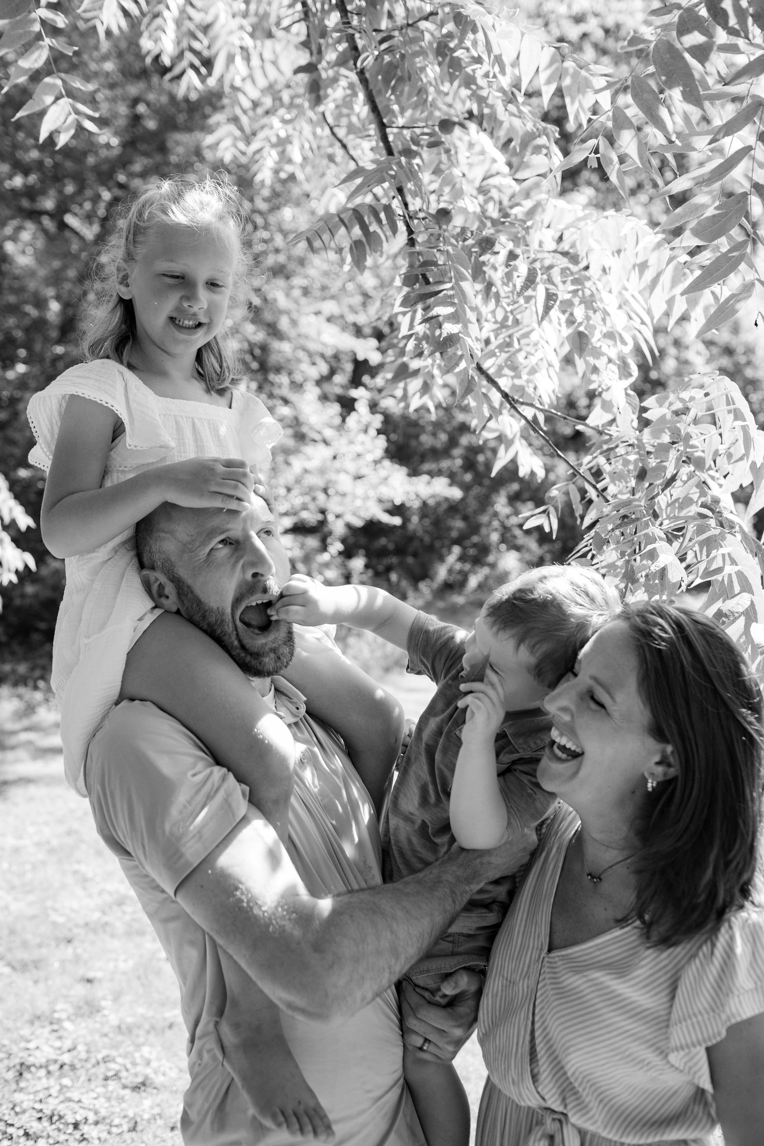 Black and white photo of a happy family spending time together outdoors under leafy trees on a sunny day.