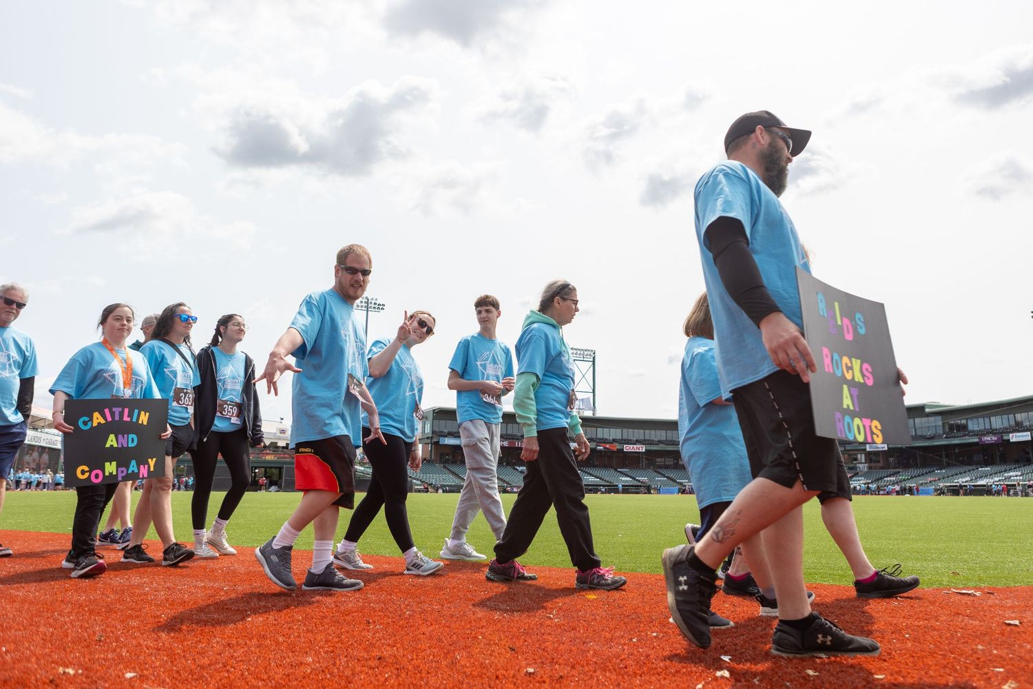 Group in light blue shirts participating in outdoor activities on a baseball field.
