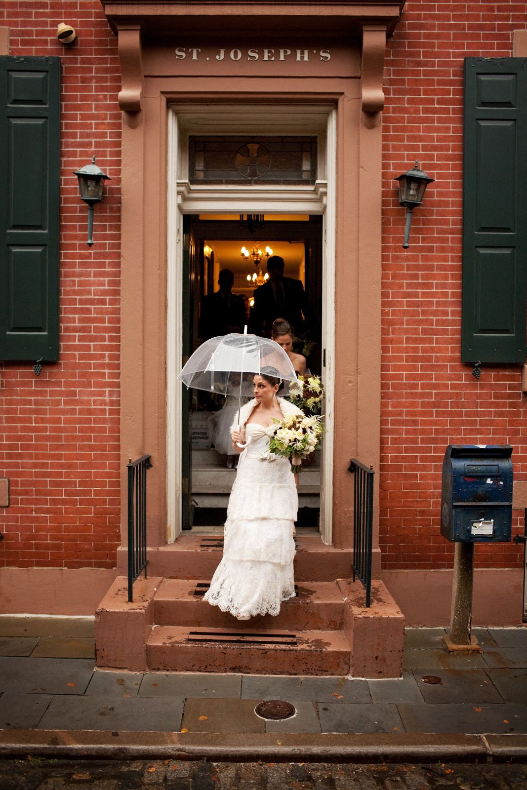 Wedding scene outside St. Joseph's historic brick building with white dress and umbrella details against red walls.