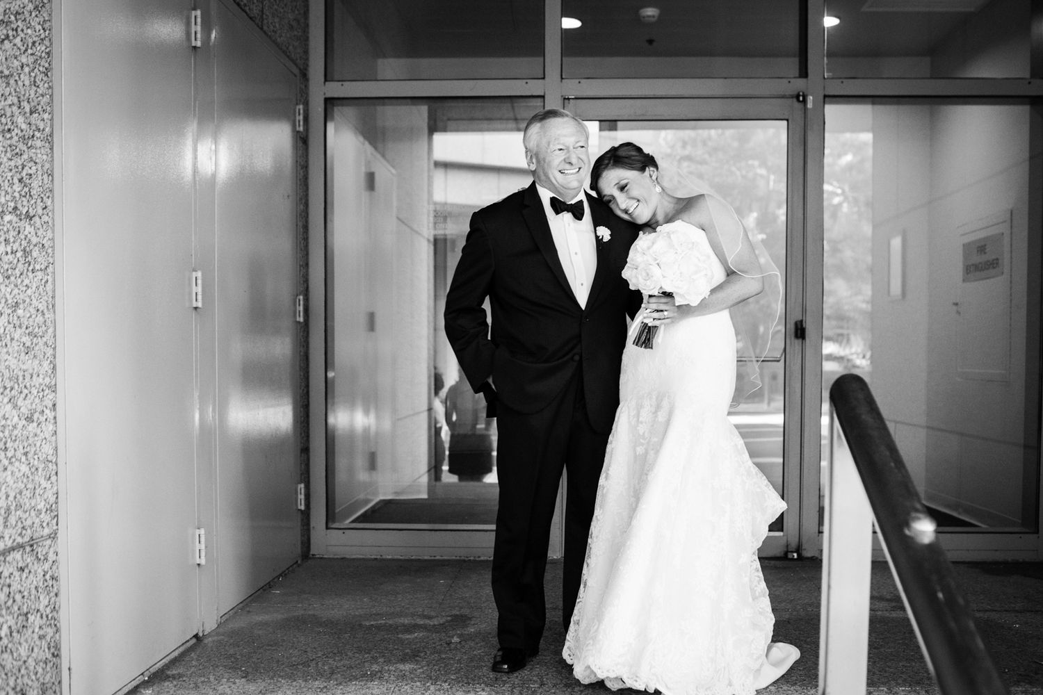 A couple in black tie and white wedding attire pose together in an elegant hallway entrance.