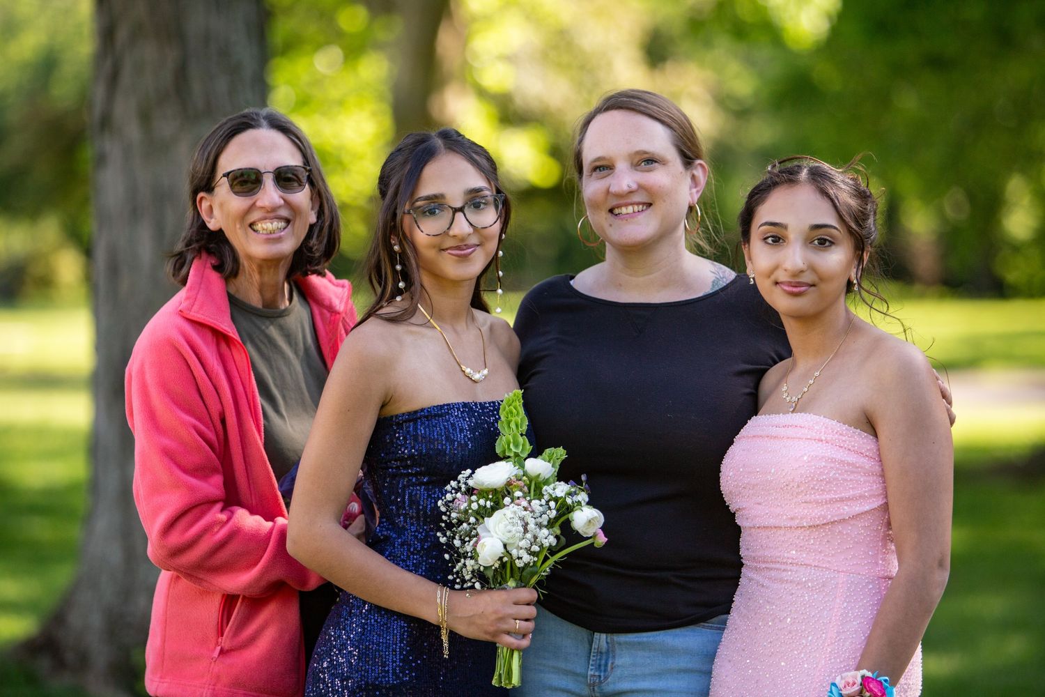 Four friends pose together outdoors on a sunny day, with one holding a bouquet of white flowers.