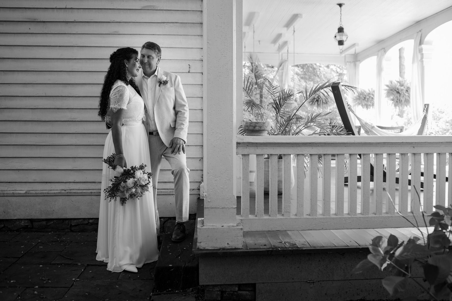 Black and white wedding portrait taken on rustic farmhouse porch with white railing.