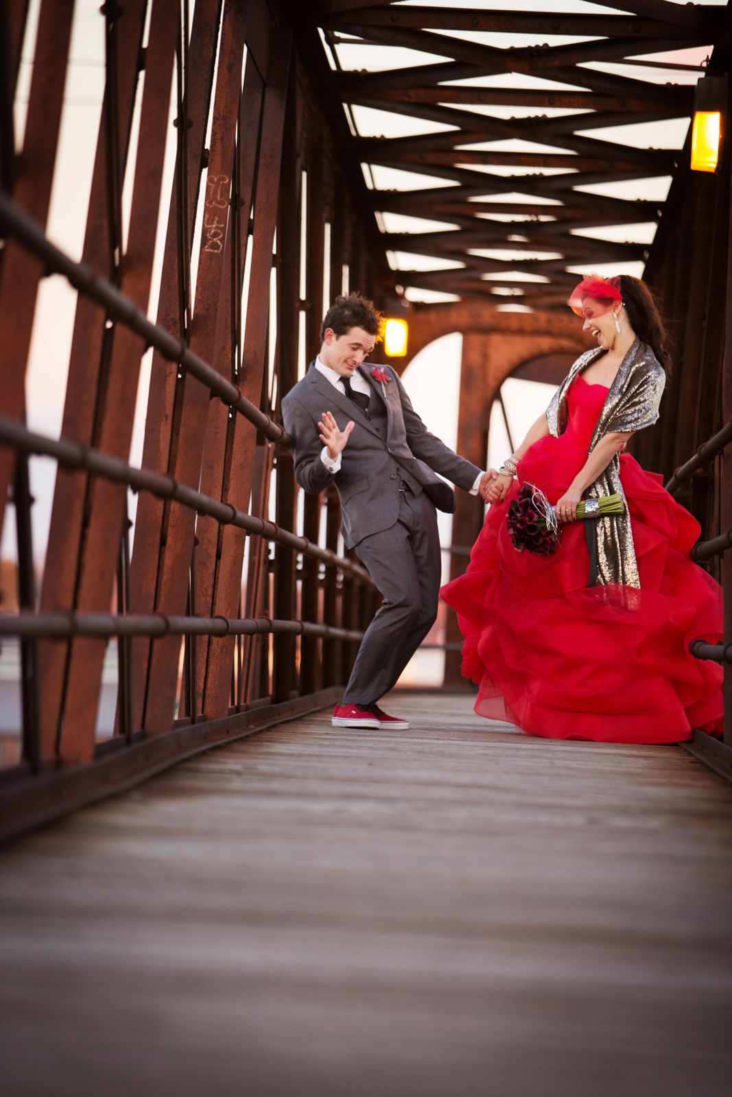 A couple dances together on a covered wooden bridge, with the woman wearing a flowing red dress and the man in a suit.