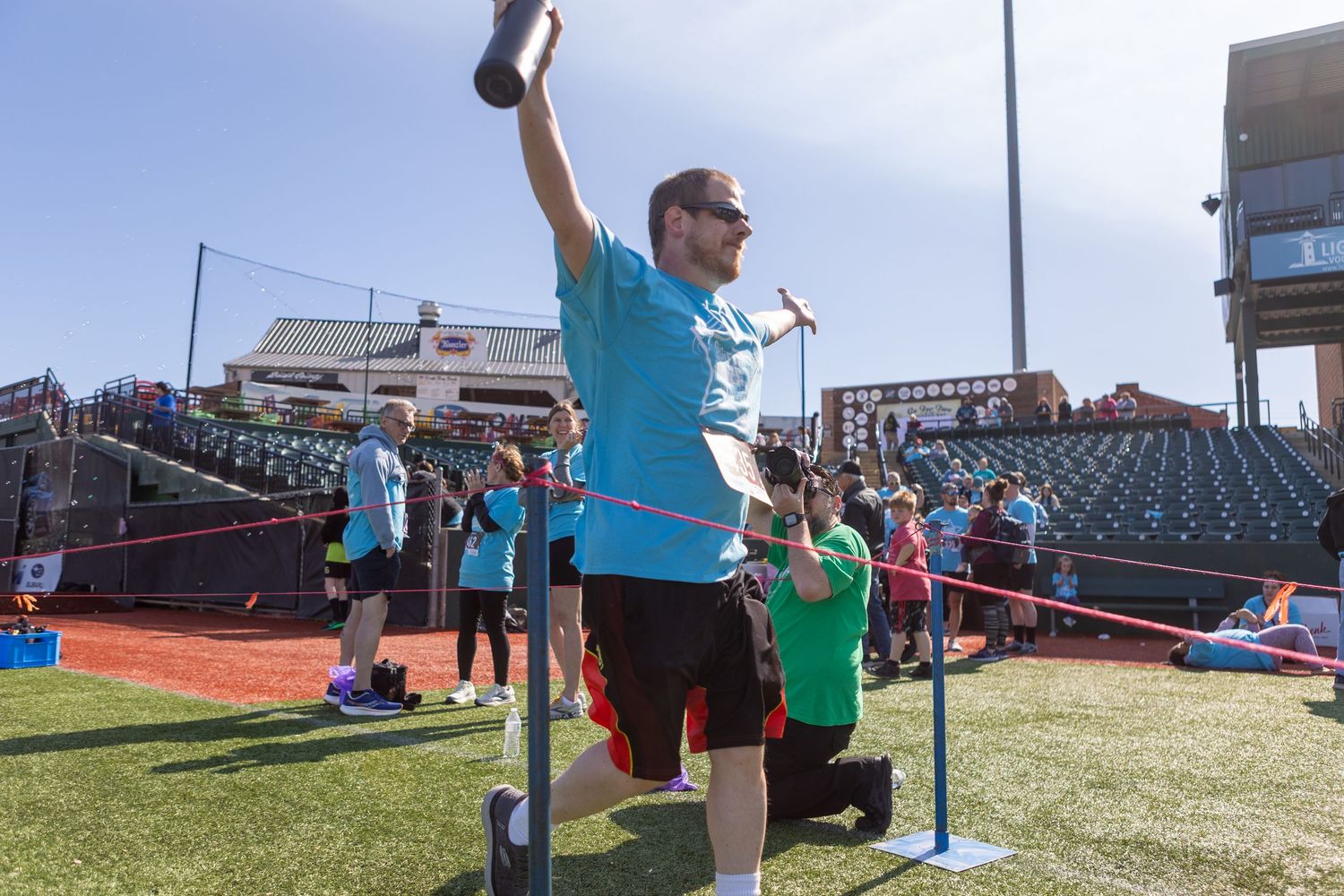 Participant celebrating with raised arms during outdoor sports event on baseball field.
