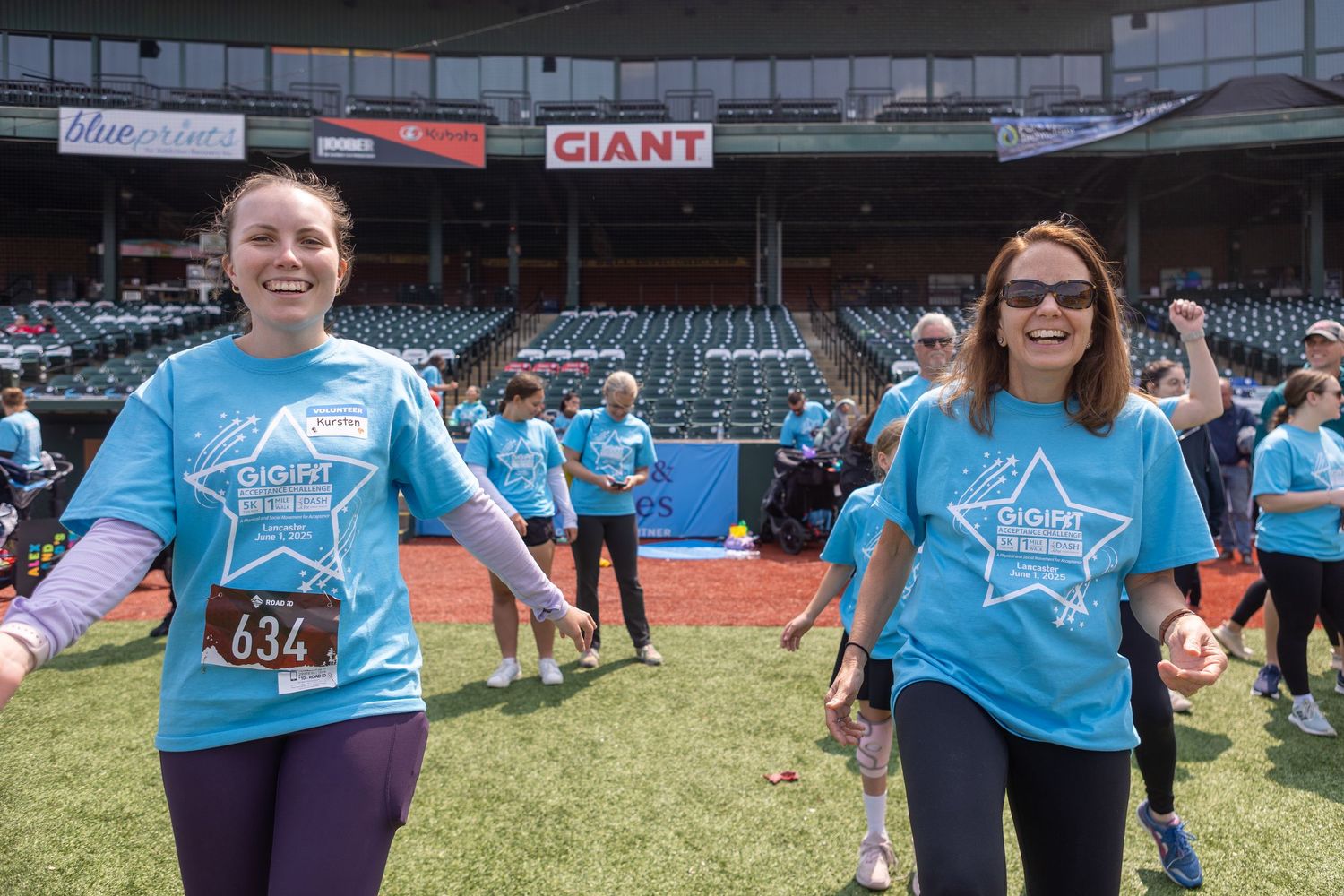 Participants wearing matching light blue t-shirts enjoy an outdoor event at a baseball stadium.