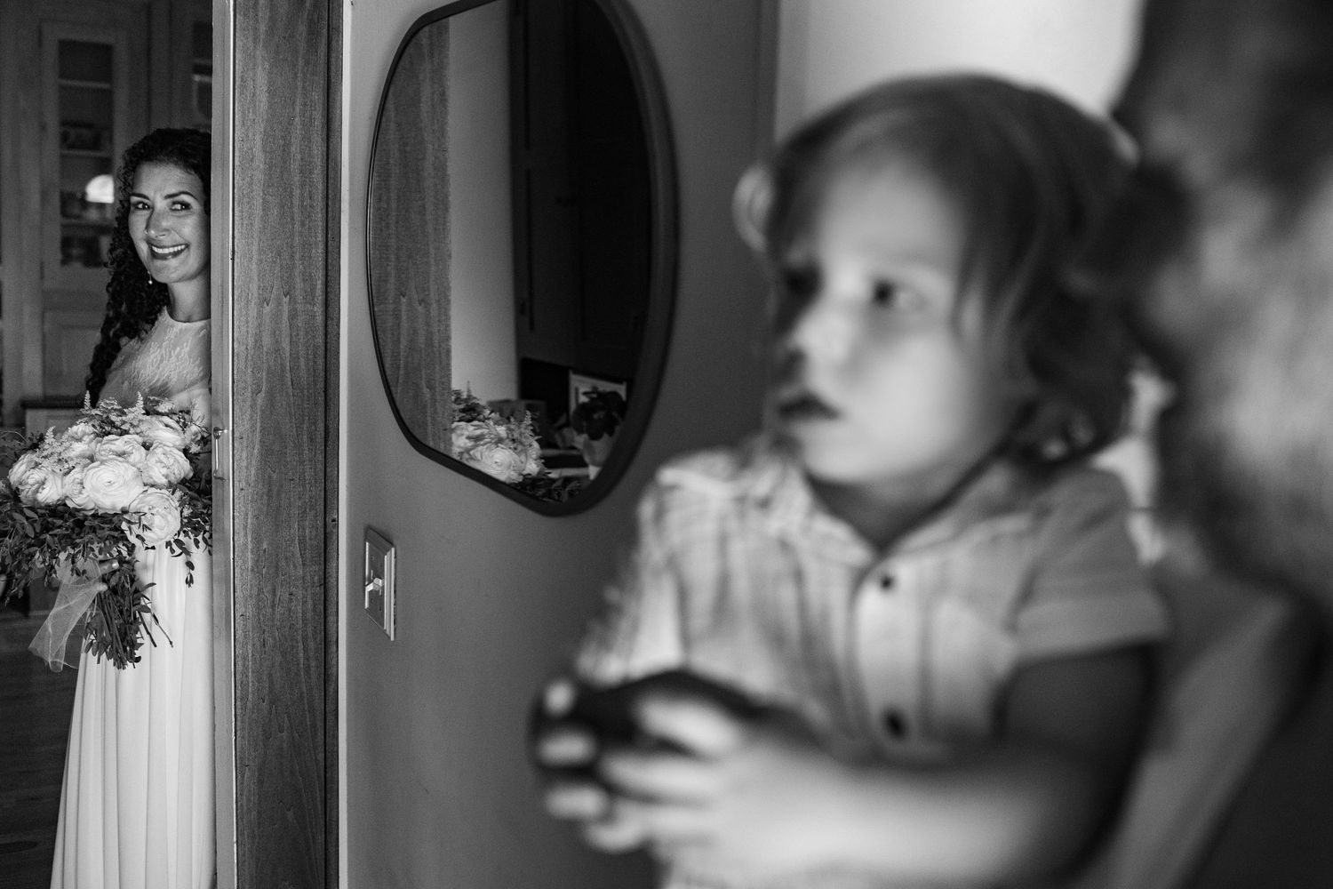 Black and white wedding photo capturing emotional pre-ceremony moments through doorway reflections.