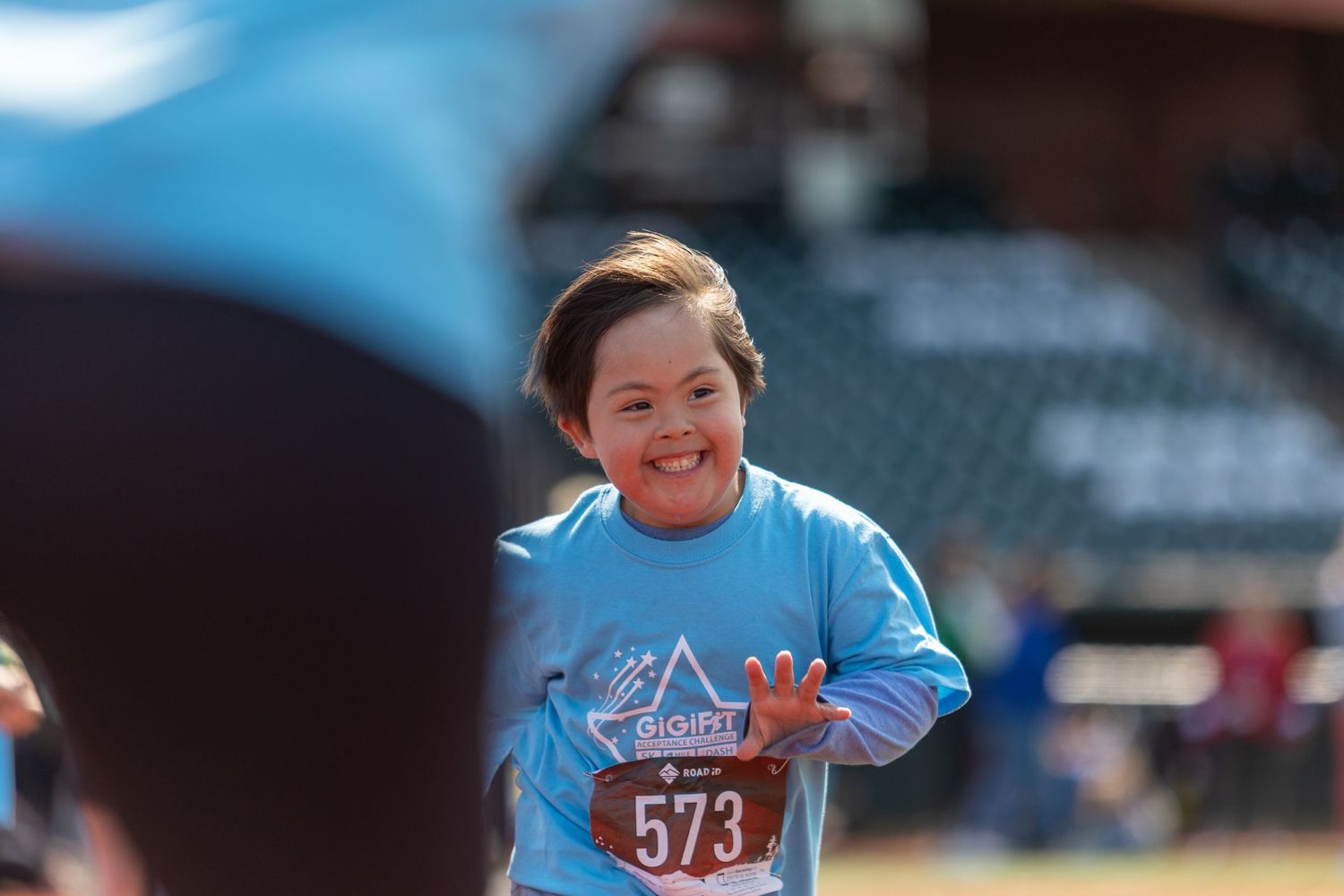 Participant wearing blue shirt with race number running on baseball field.