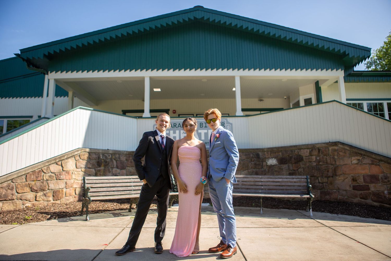 Three people pose together outside a building with a green roof and white stone steps.