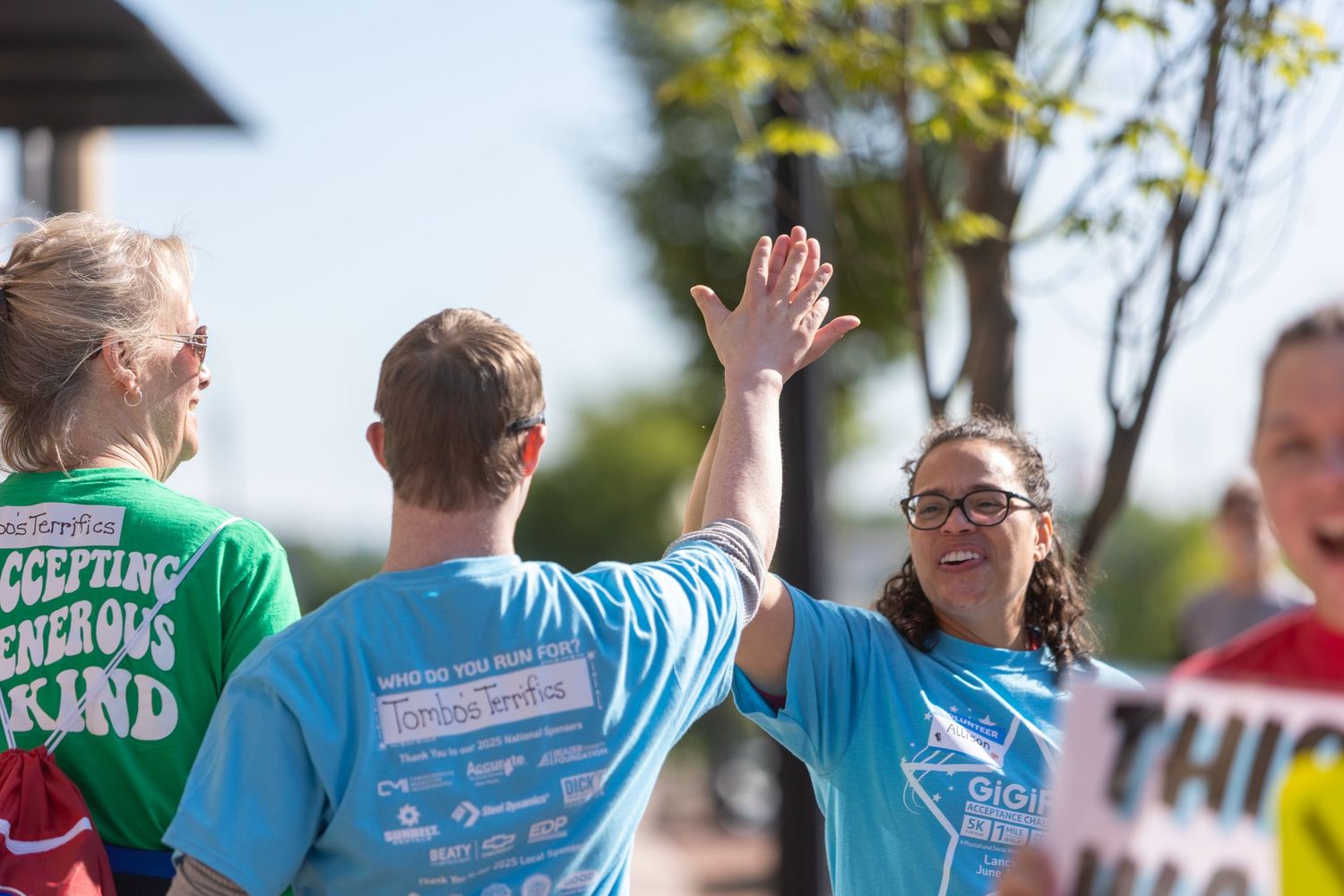 Participants in matching blue t-shirts give high fives during an outdoor charity walk or race event.