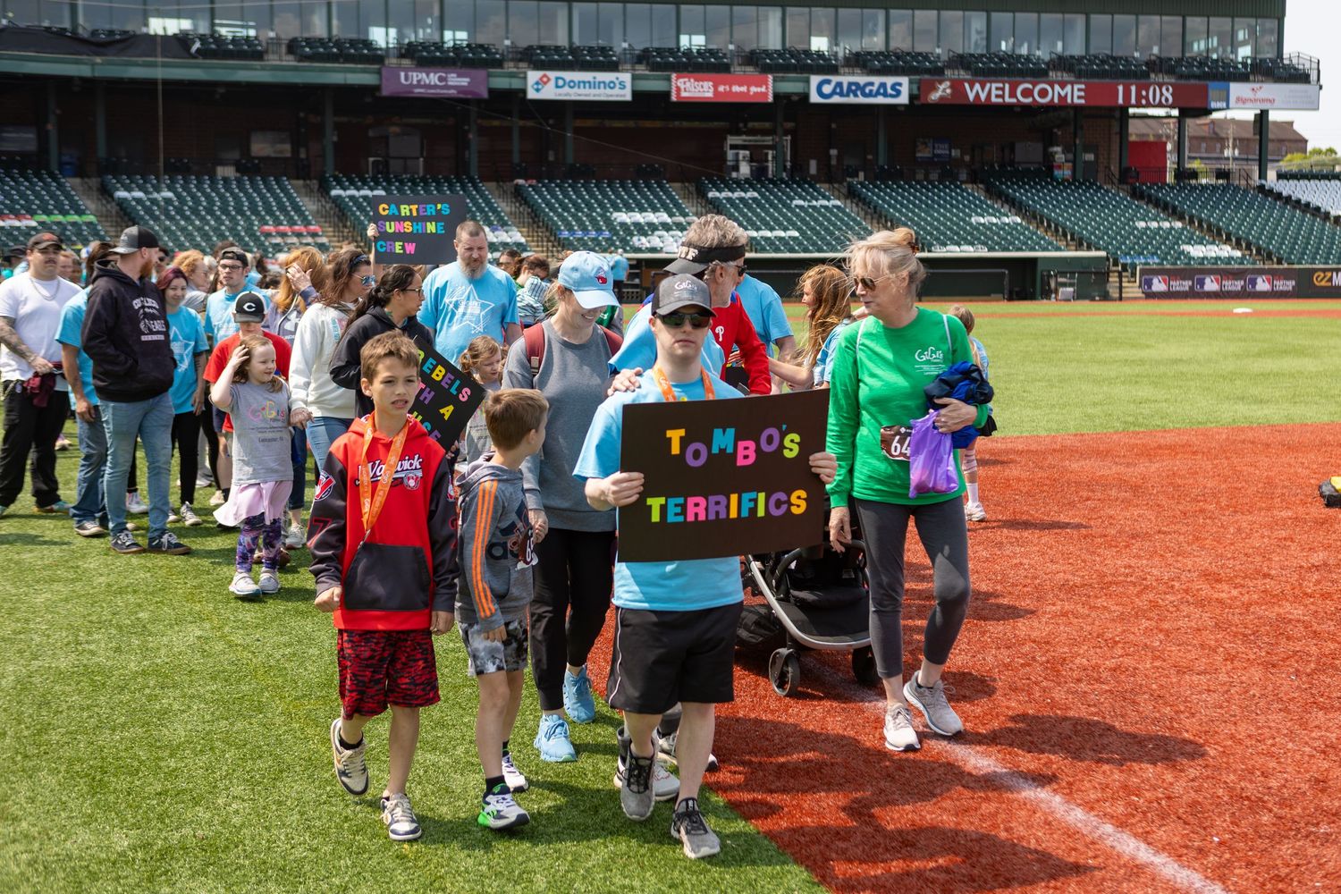 Participants walking along baseball field warning track during community event.