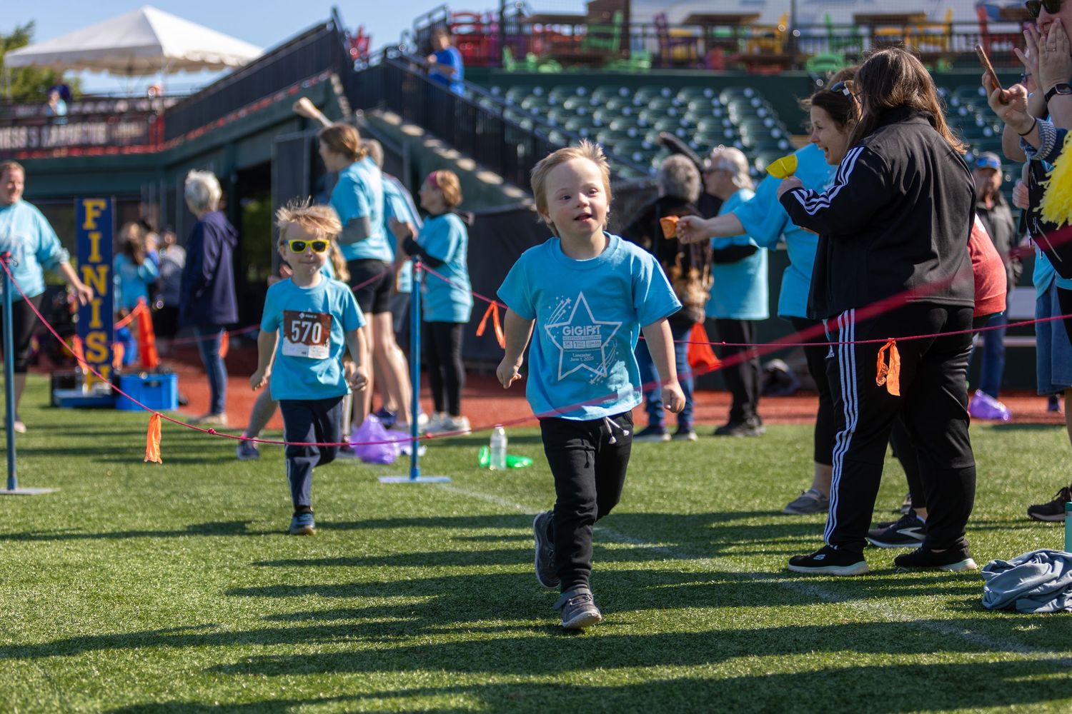 Participants in light blue shirts run through an activity course at a baseball stadium.