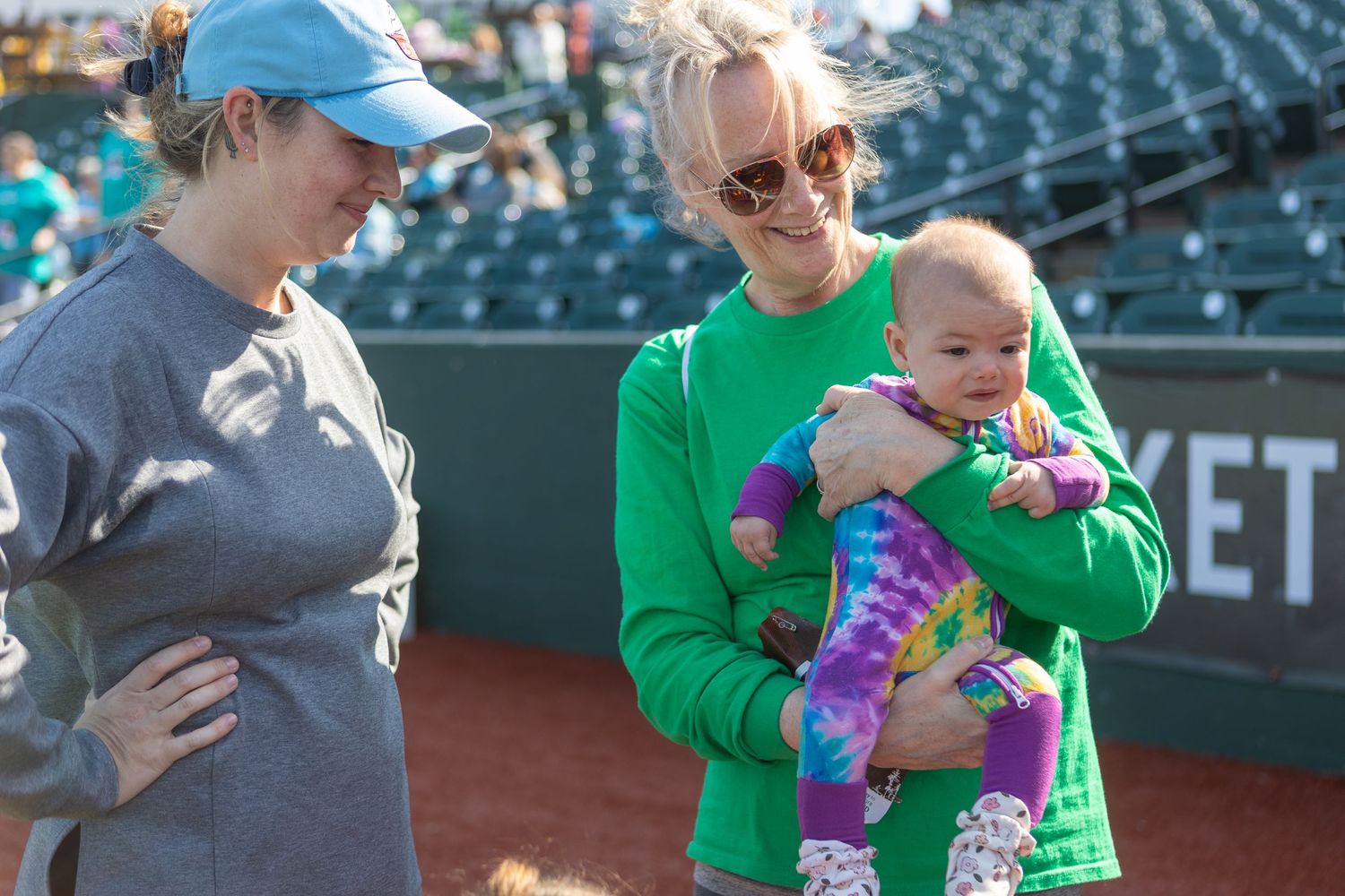 Group gathers on baseball field with infant during daytime event.