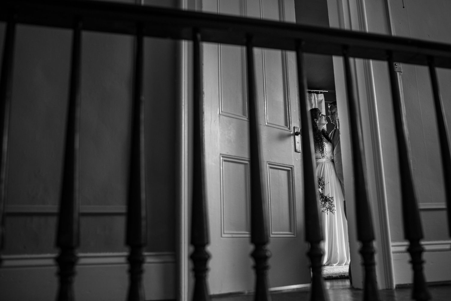 Dramatic black and white stairwell photo showing wedding dress through bannister shadows.