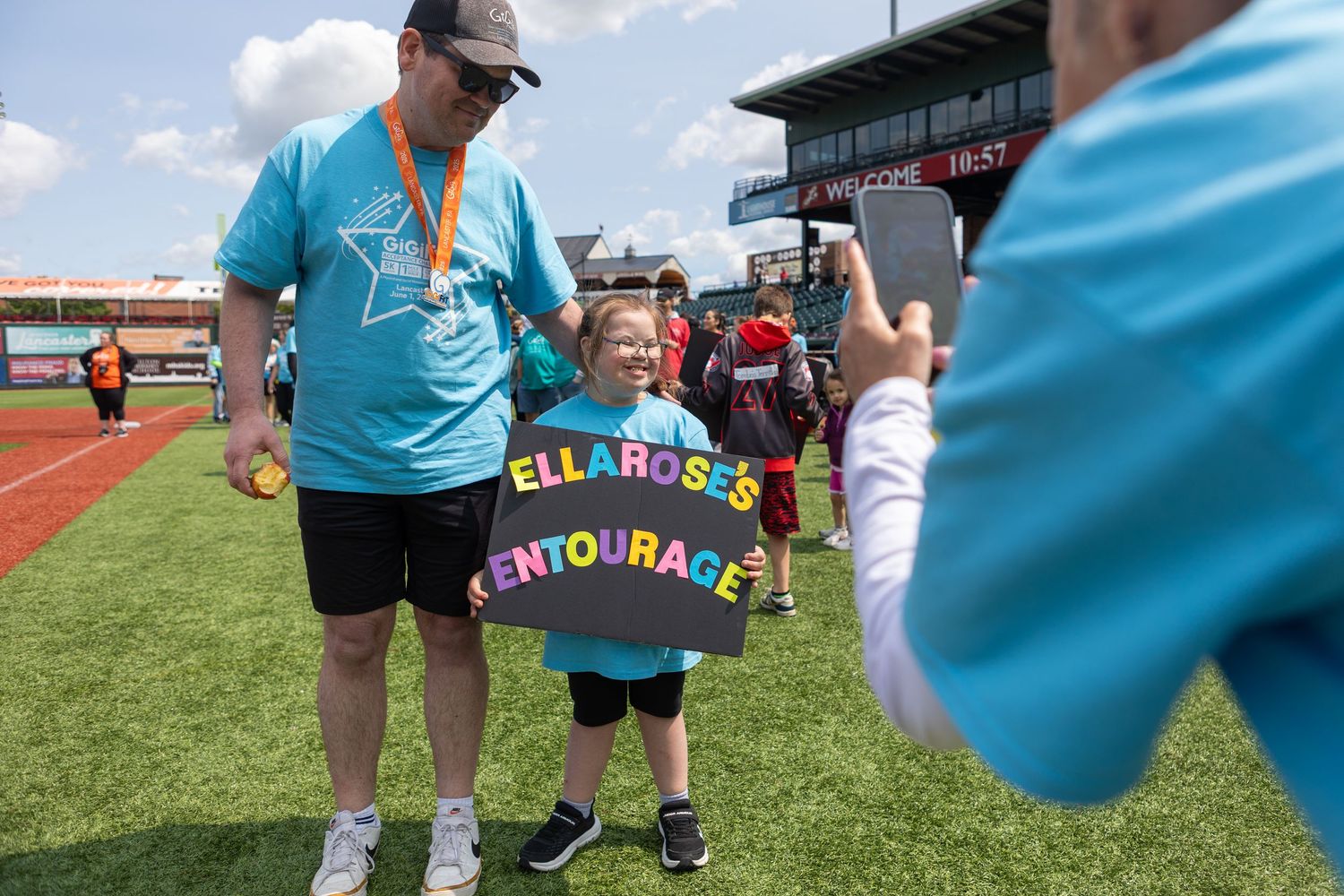 Child wearing colorful rainbow encouragement sign at outdoor sporting event with supporter.