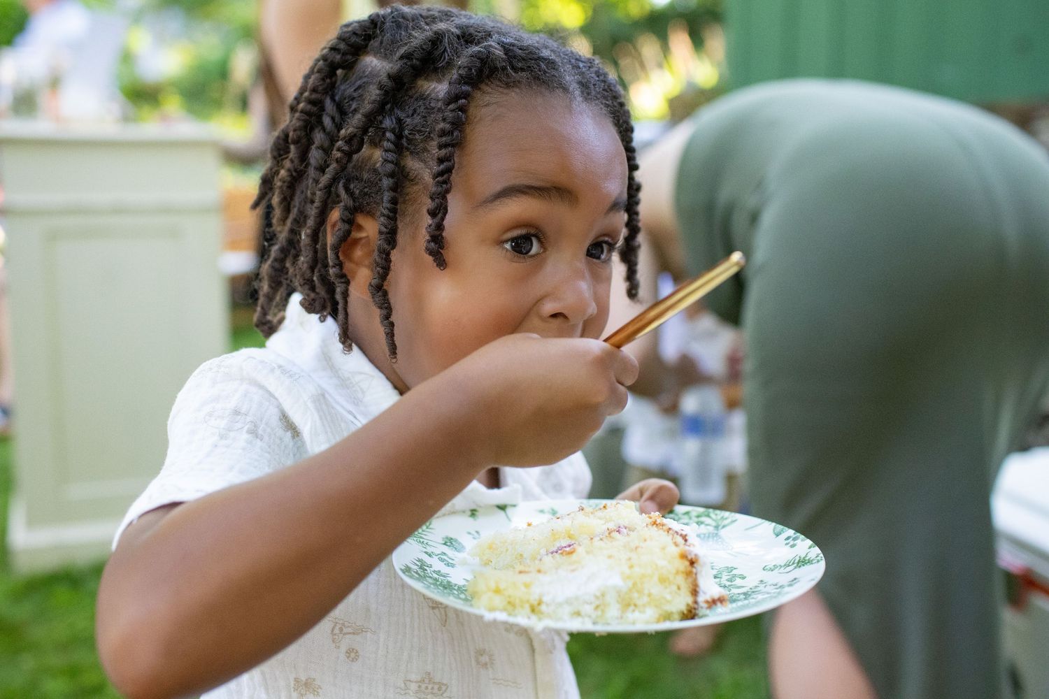 Young guest with braided hair enjoying a plate of food at an outdoor gathering.