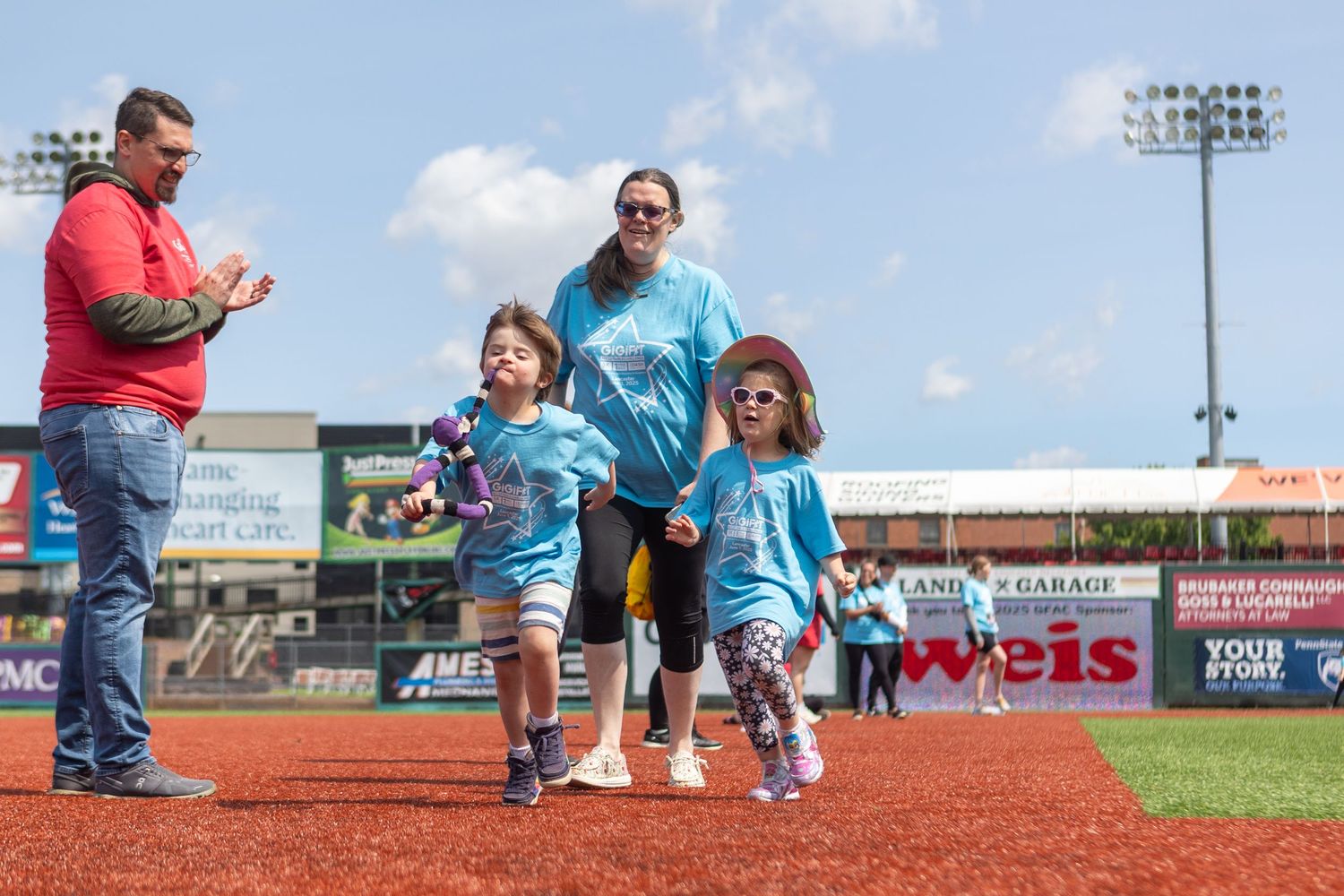 Families in matching blue shirts participate in activities on a baseball field's warning track.