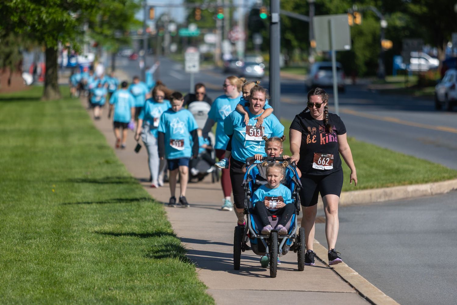 Group of runners in matching blue shirts participate in a charity race along a tree-lined street.