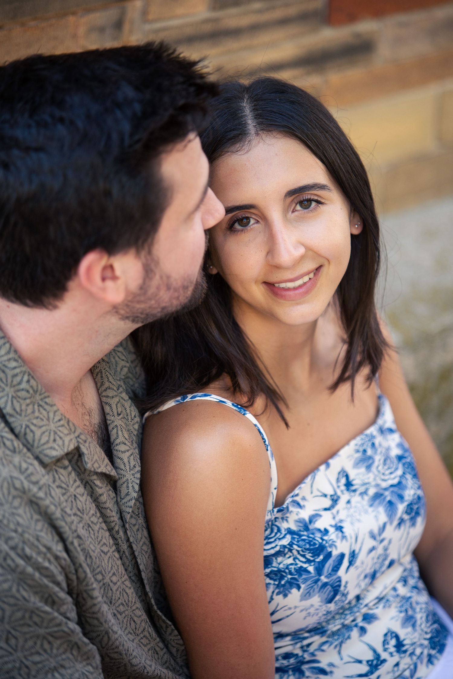 A couple in a romantic outdoor setting with a person wearing a blue and white patterned dress sitting close together.