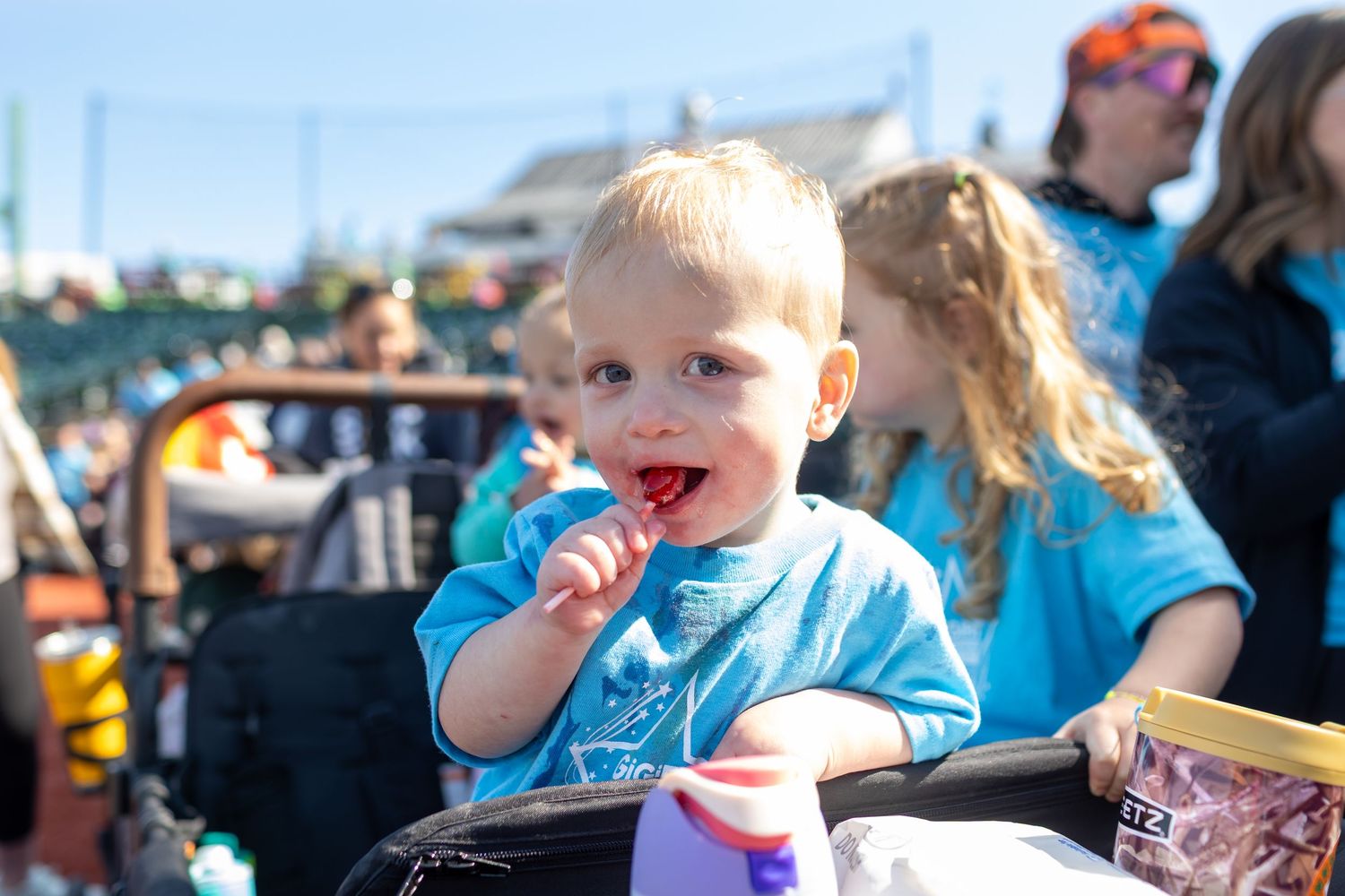 A young participant in a light blue shirt enjoys a snack during an outdoor event.