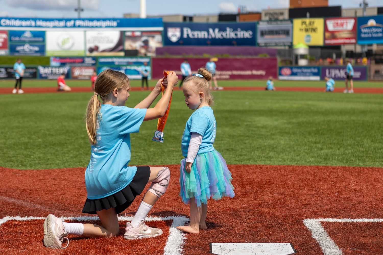 Two participants in matching blue tutus high-five on baseball field baseline.