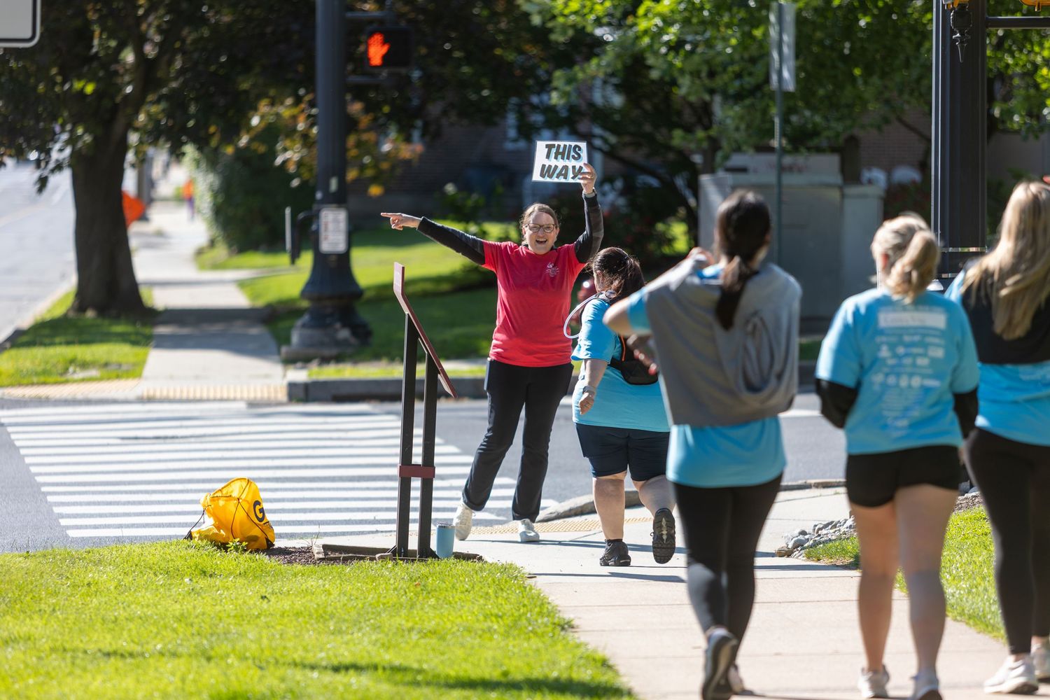 Participants in light blue shirts cheer and wave during an outdoor community event.