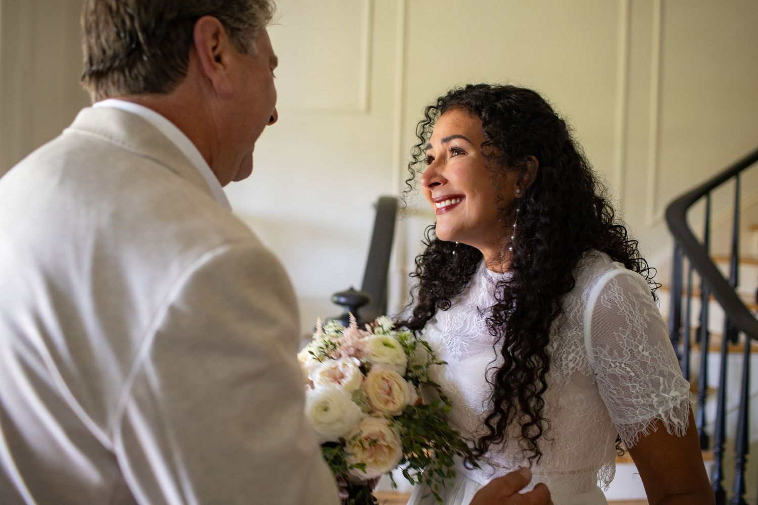 A candid moment between a bride in white lace and someone in a light-colored suit during a wedding.