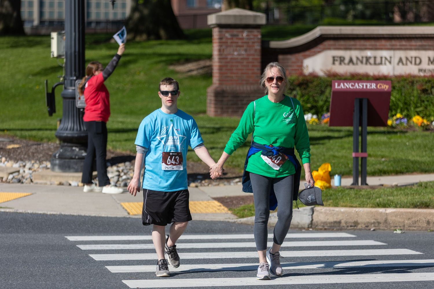 Two participants walk together on a crosswalk during an outdoor event.