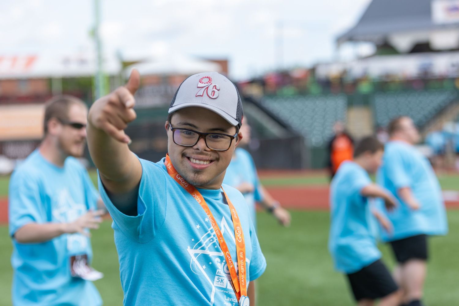 Participant in light blue shirt giving thumbs up during baseball stadium charity event.