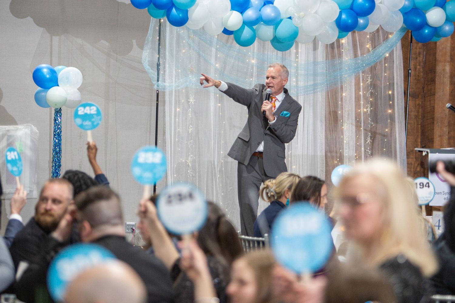 Event celebration with blue and white balloons decorating the ceiling as attendees raise glasses during a toast.