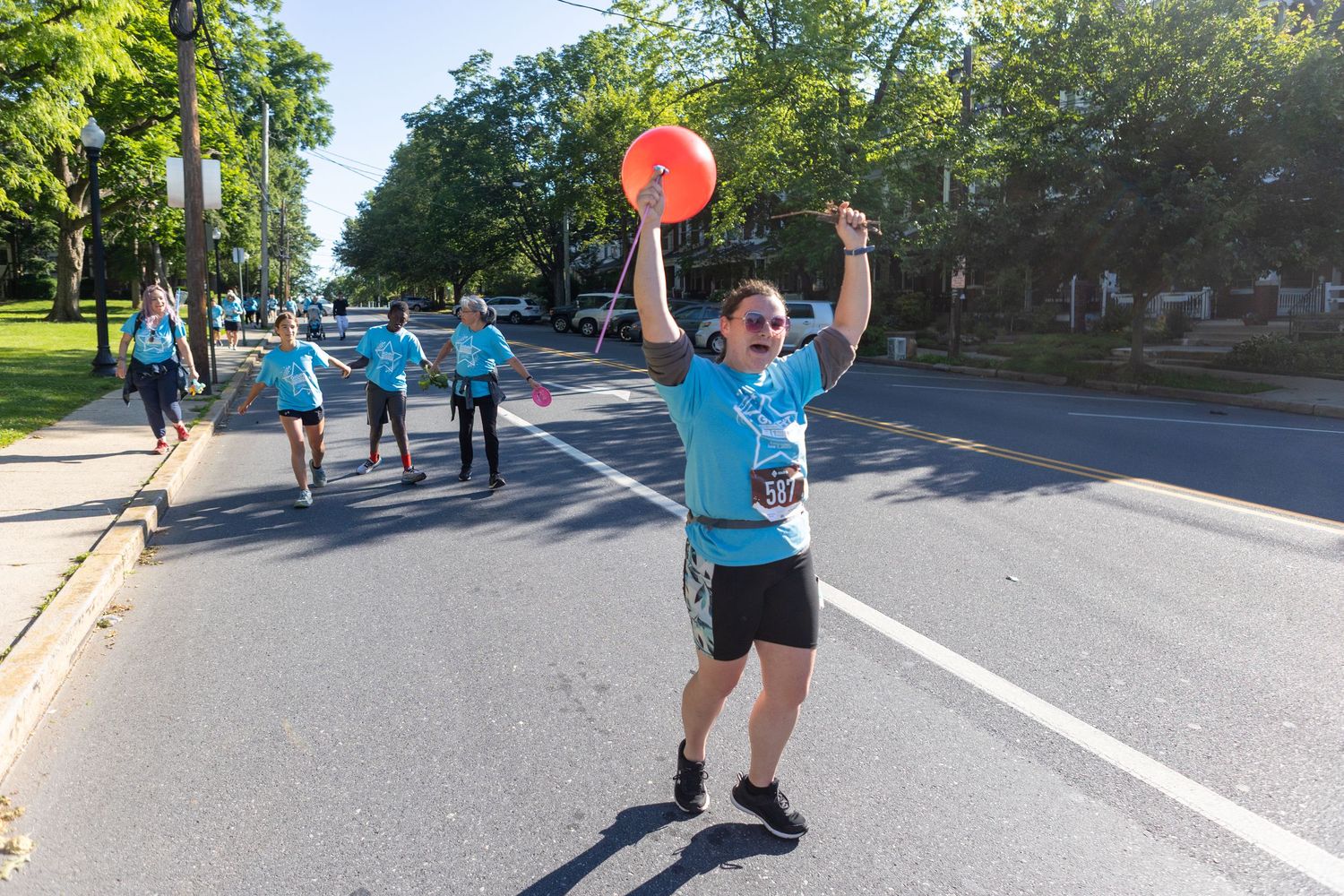 Participant in light blue shirt celebrates with raised arms during outdoor community event.
