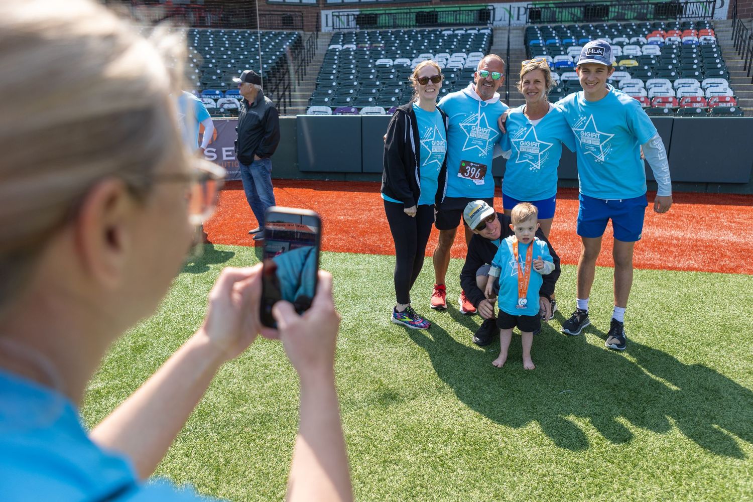People wearing matching blue shirts pose for a photo on a baseball field.
