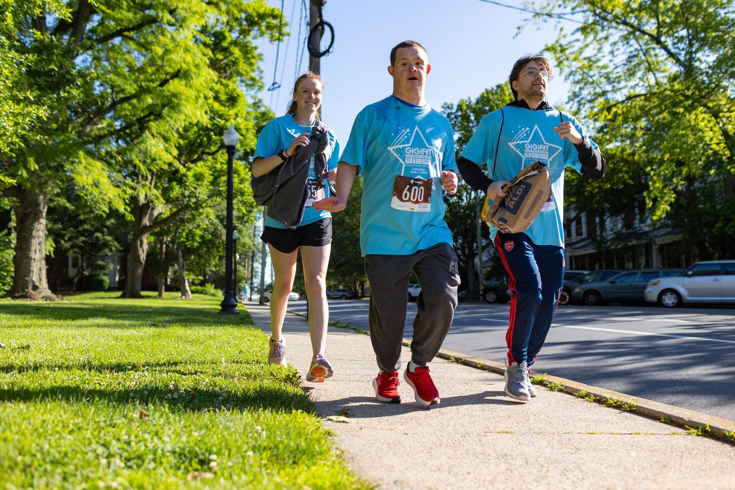 Group walking along a sidewalk wearing matching blue shirts during a community gathering.