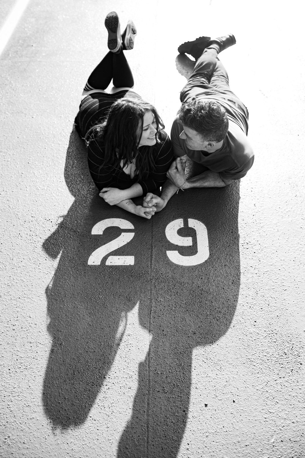 Black and white photo of couple lying on pavement with number 29 and shadows.