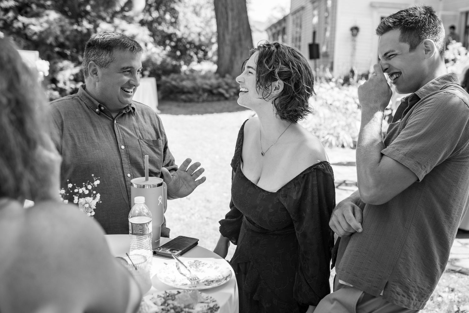 Black and white photo showing guests having an animated conversation at an outdoor social gathering.