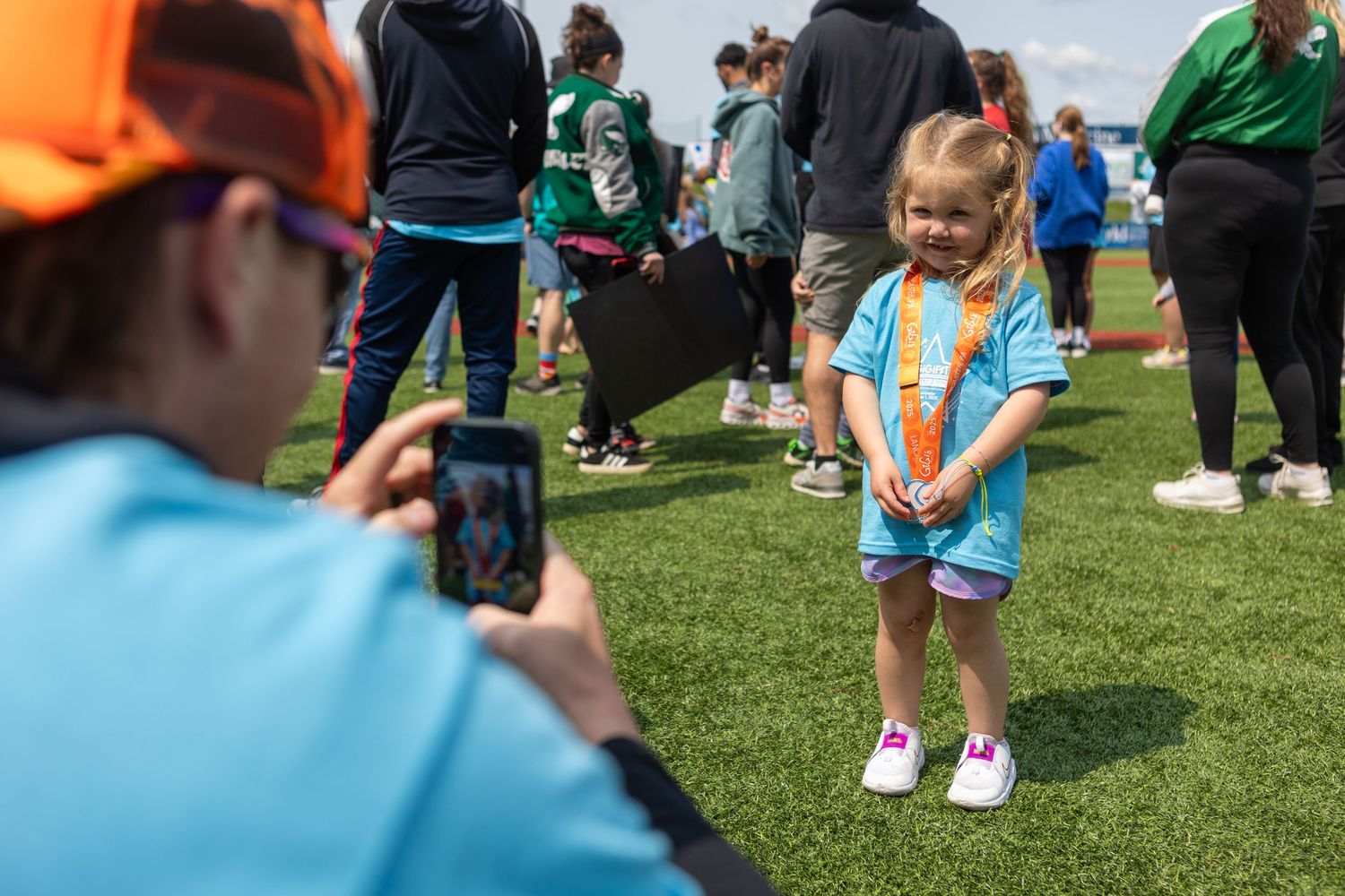 A photographer takes a photo of a young participant in a light blue shirt at an outdoor sports event.