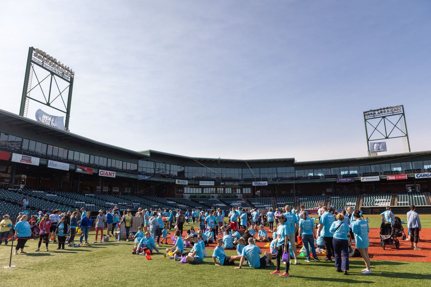 Large group of participants in blue shirts gather on a baseball field under stadium lights.