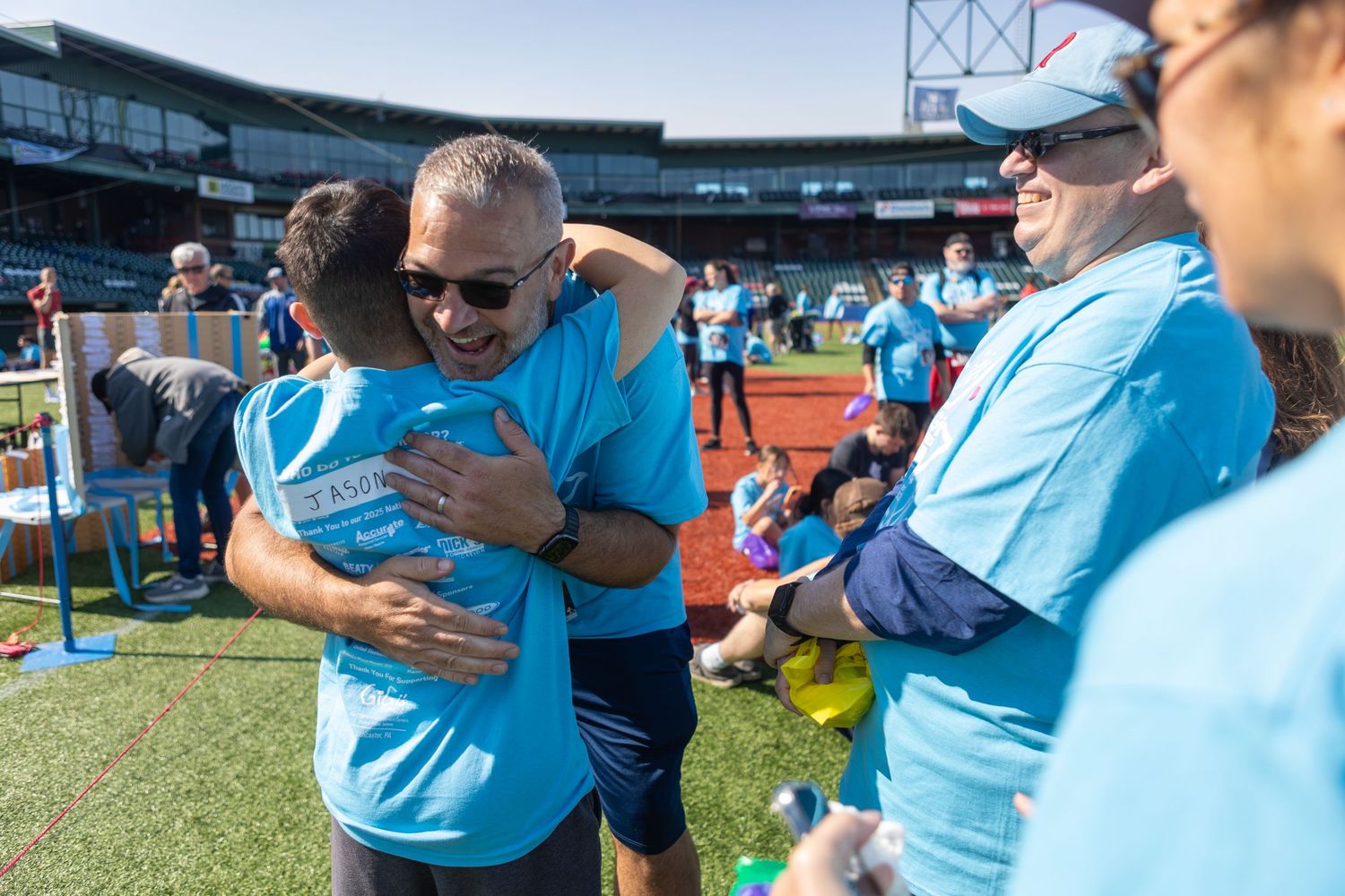 People wearing matching blue shirts embrace during an outdoor community event.