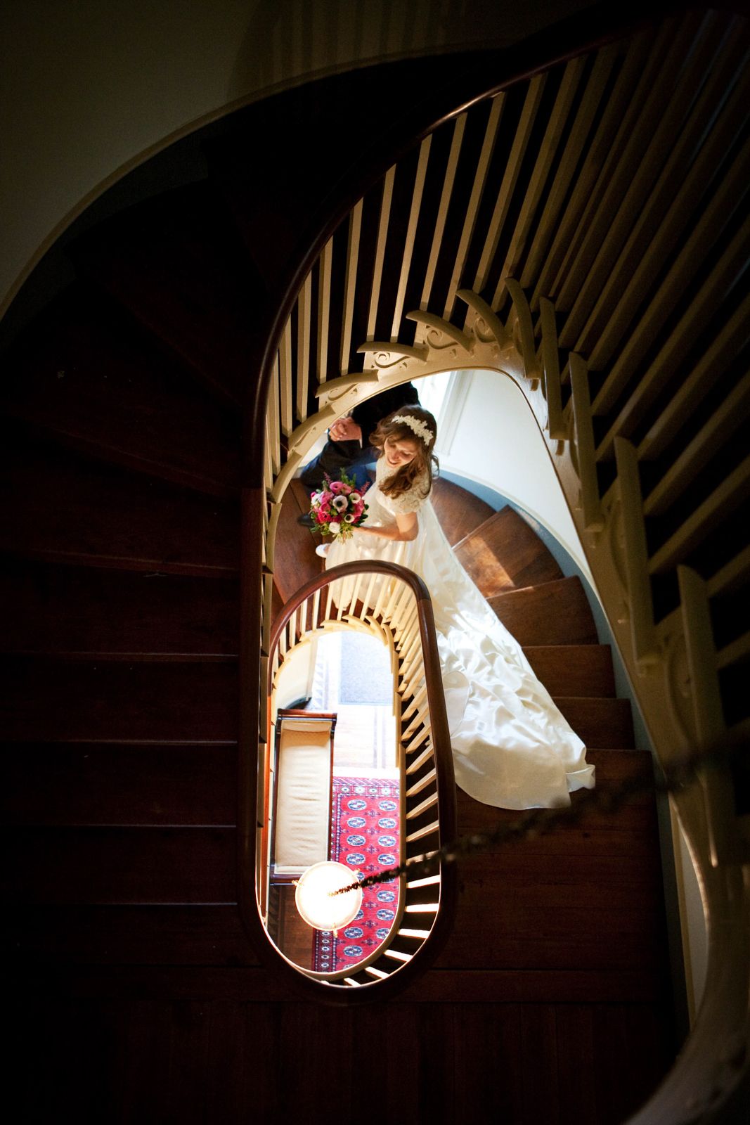 Looking down a spiral wooden staircase with a wedding couple sharing an intimate moment in dramatic lighting.
