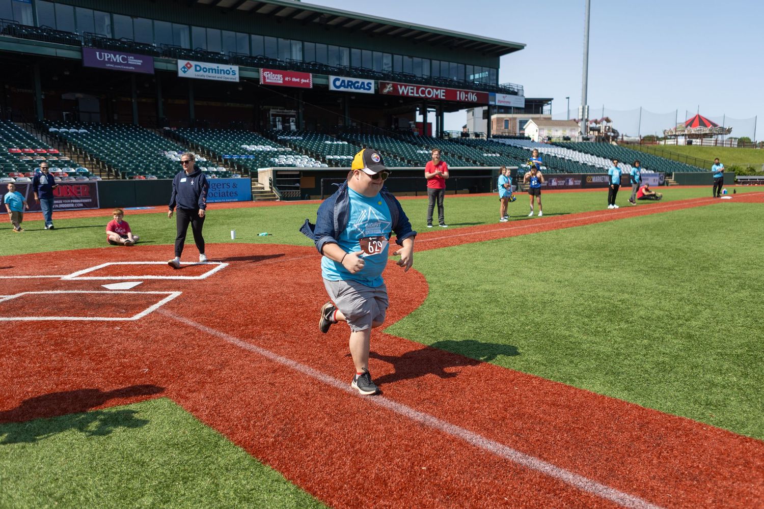 Runners cross home plate on a baseball diamond during a community event.