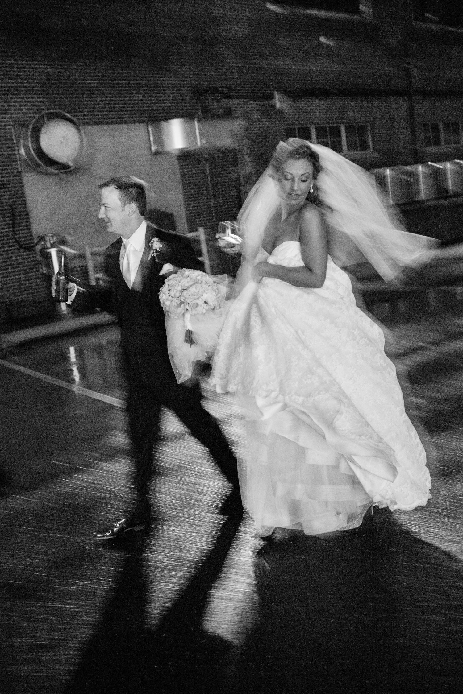 A bride in a flowing white gown and groom in a dark suit dance energetically on a polished ballroom floor.