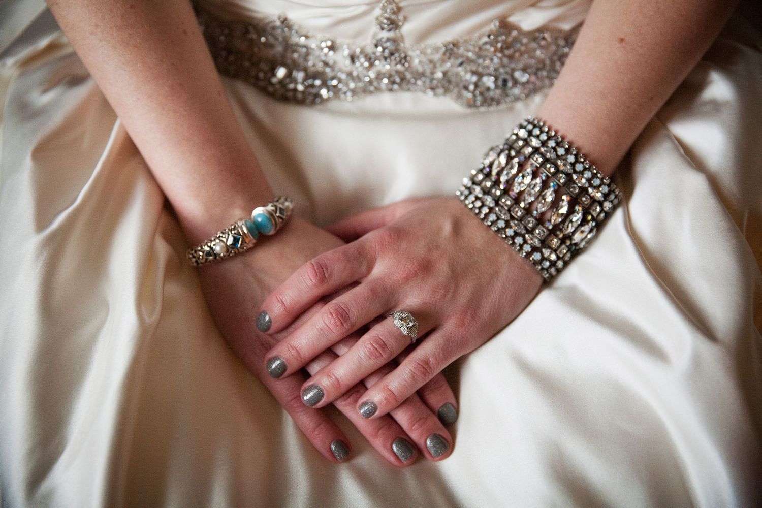 Elegant bridal hands with sparkling vintage style bracelet and ring displayed on white satin wedding dress.