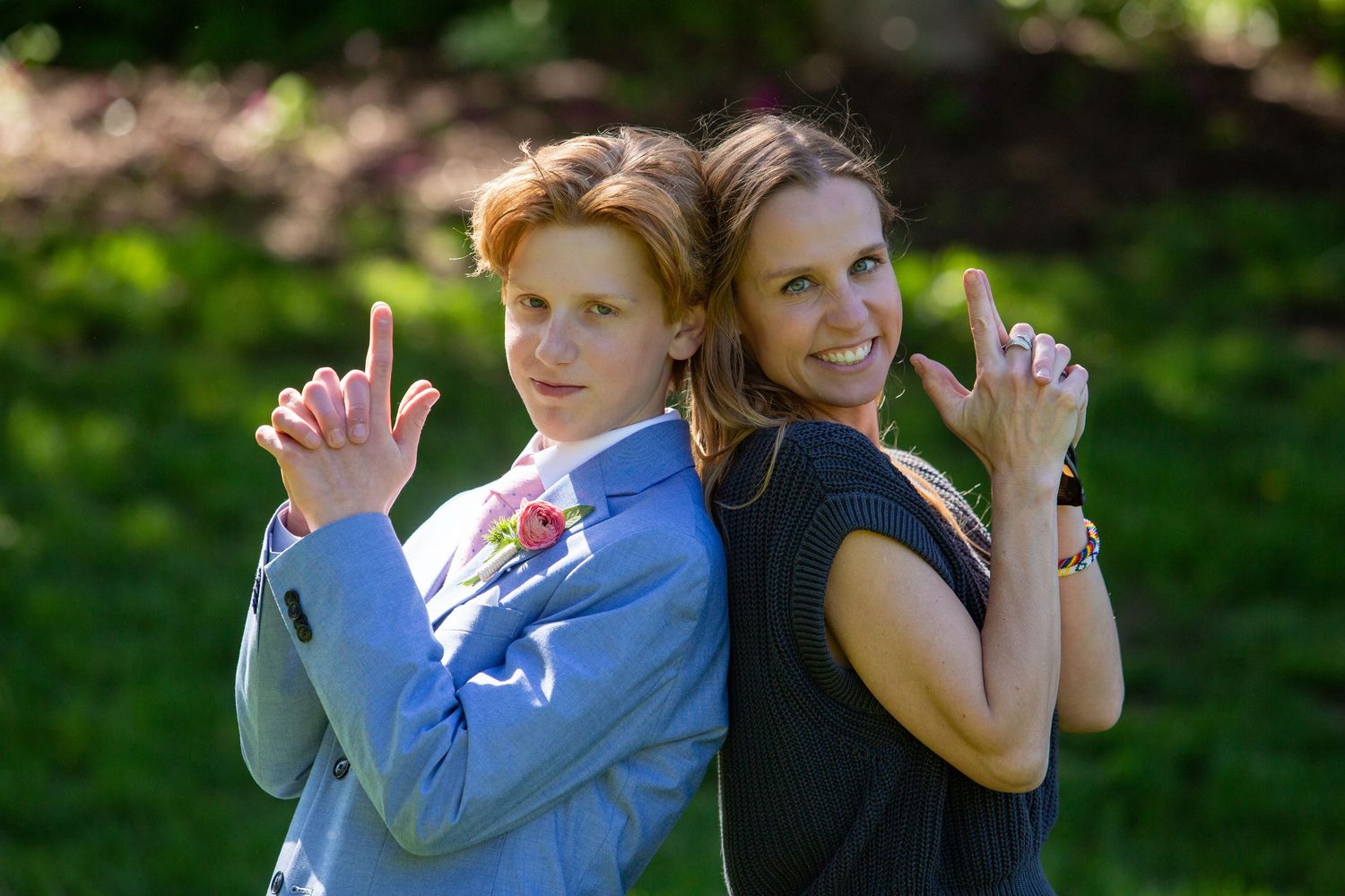 Two people standing back-to-back outdoors while playfully posing with finger guns in a sunny garden setting.