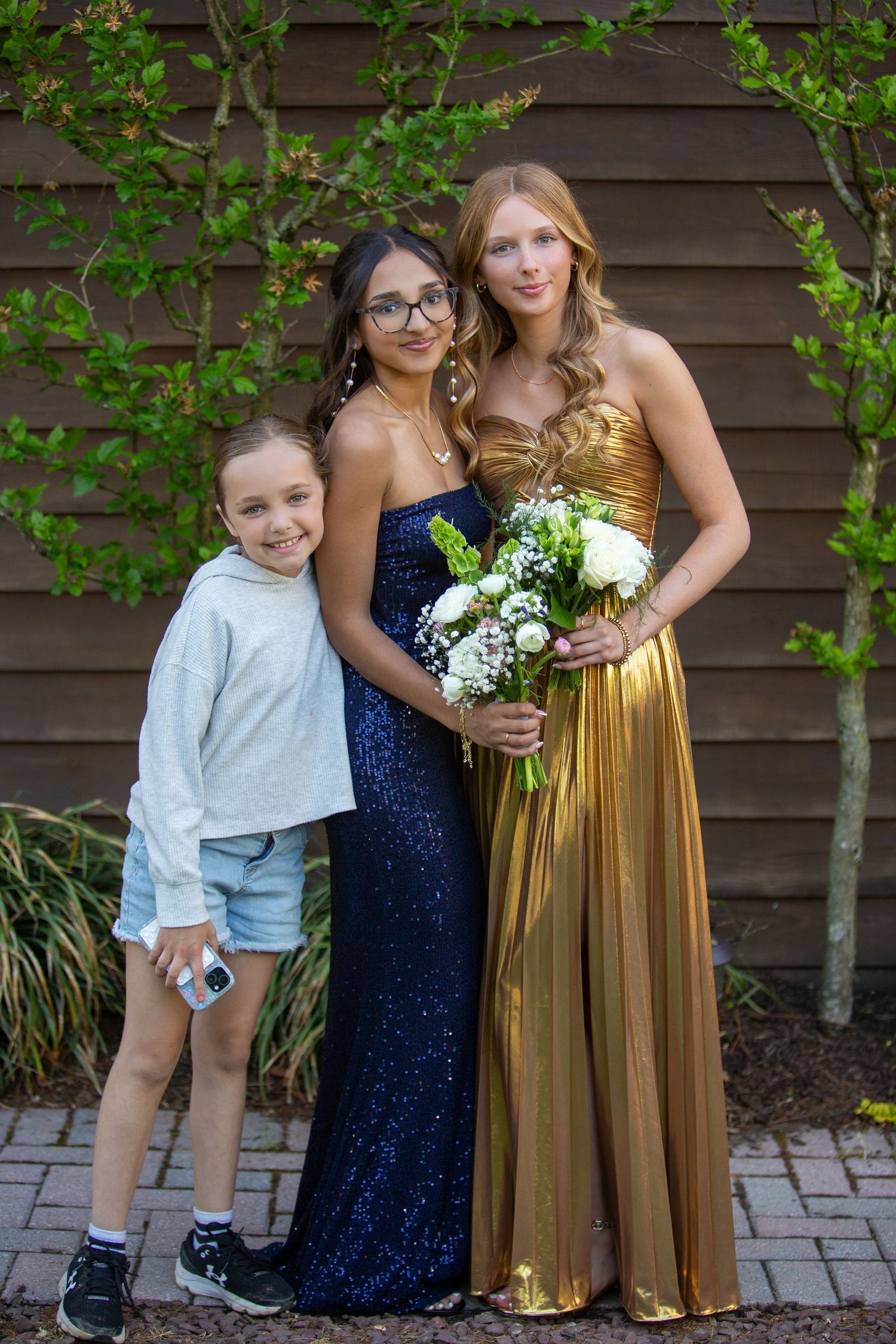A formal group photo with a young child in casual wear and two people in sparkly navy and gold evening gowns.